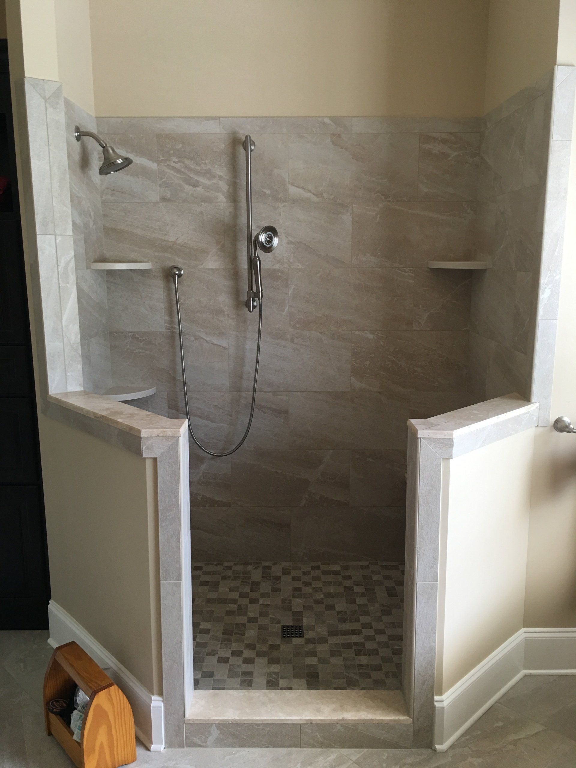 Accessible shower stall with stone tile, built-in shelves, and a handheld showerhead.