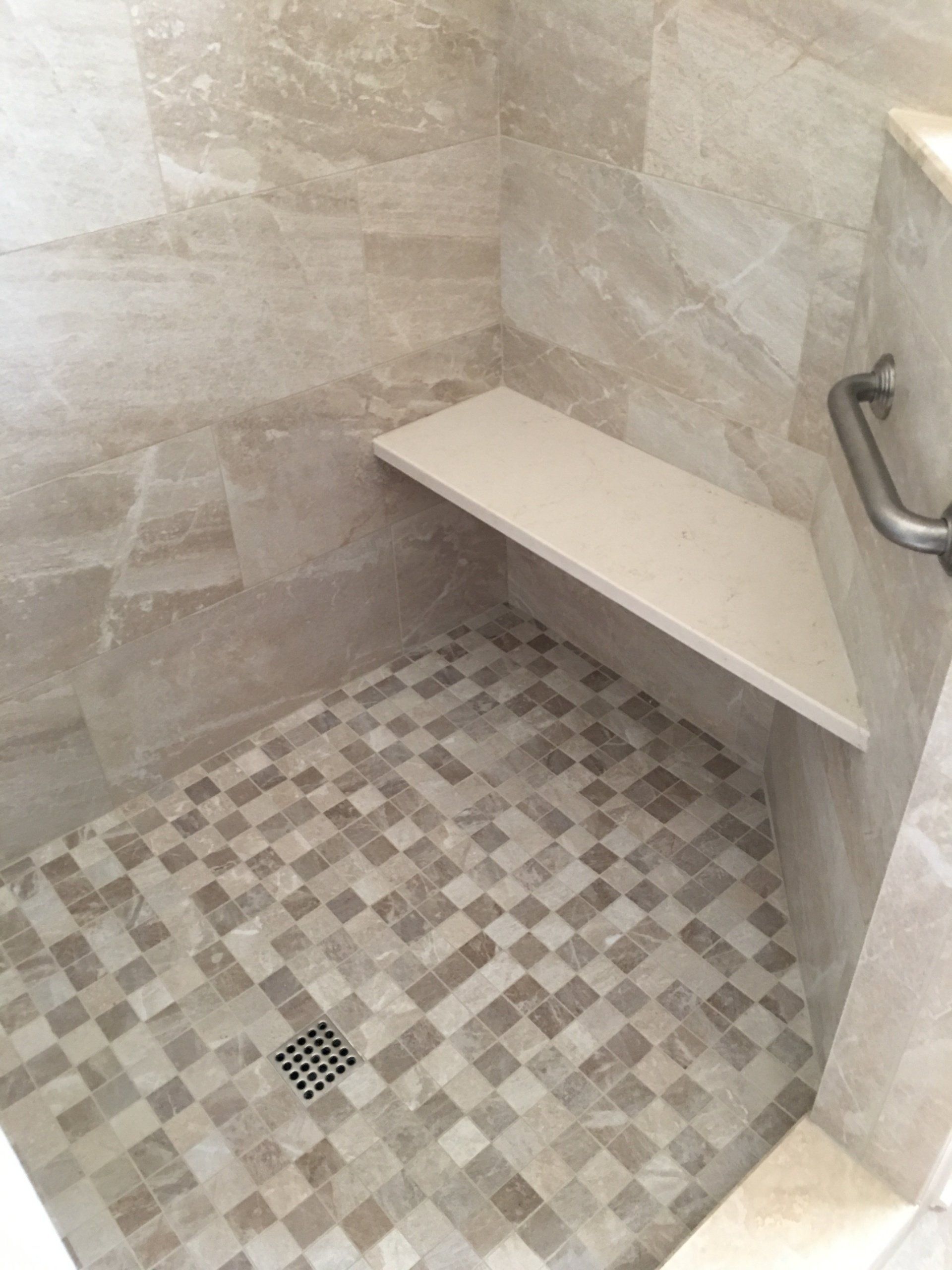 Shower with beige tile, corner seat, mosaic floor, and a silver grab bar.