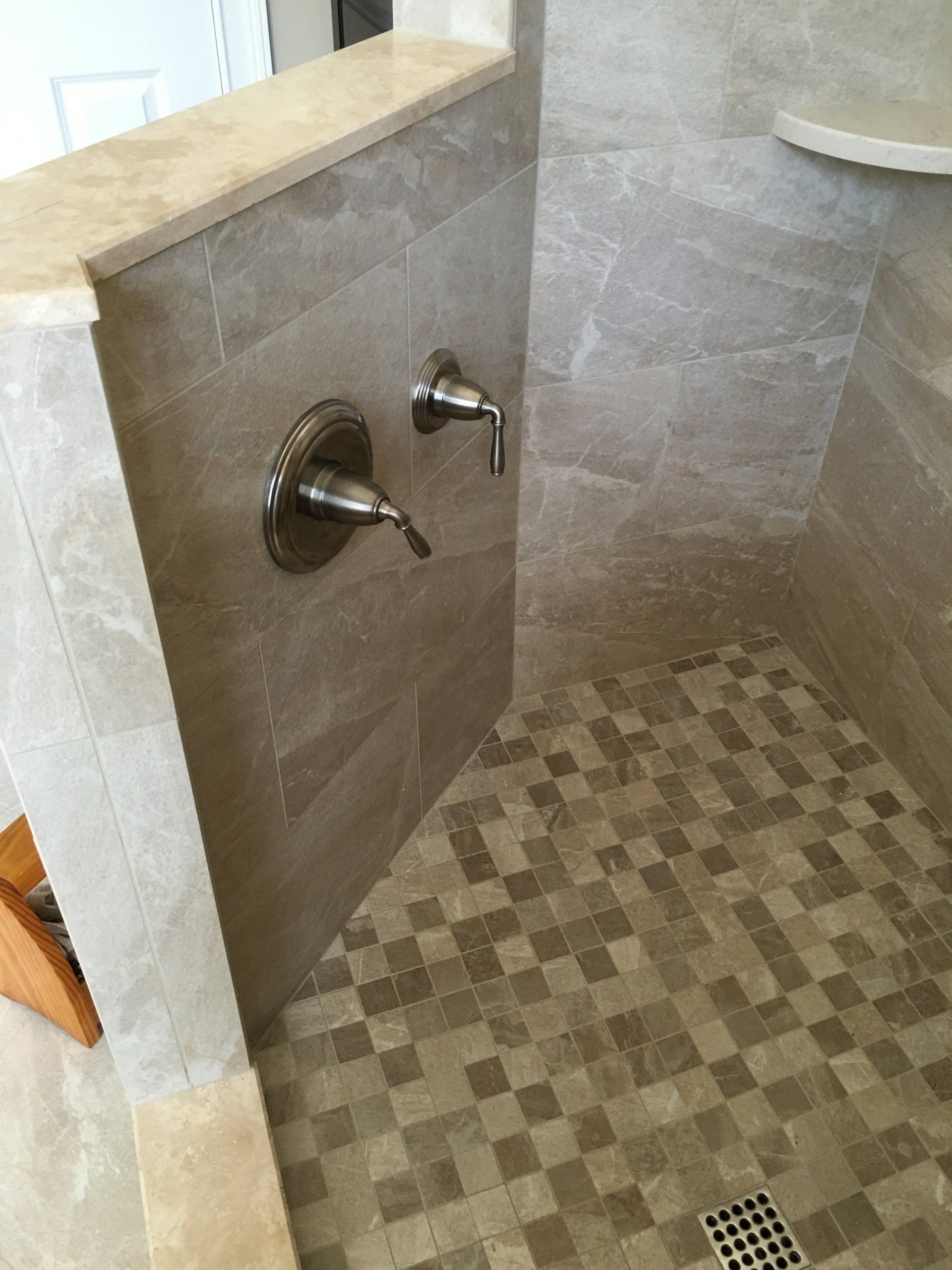 Shower stall with tan tile walls and floor. Two silver faucets are mounted.