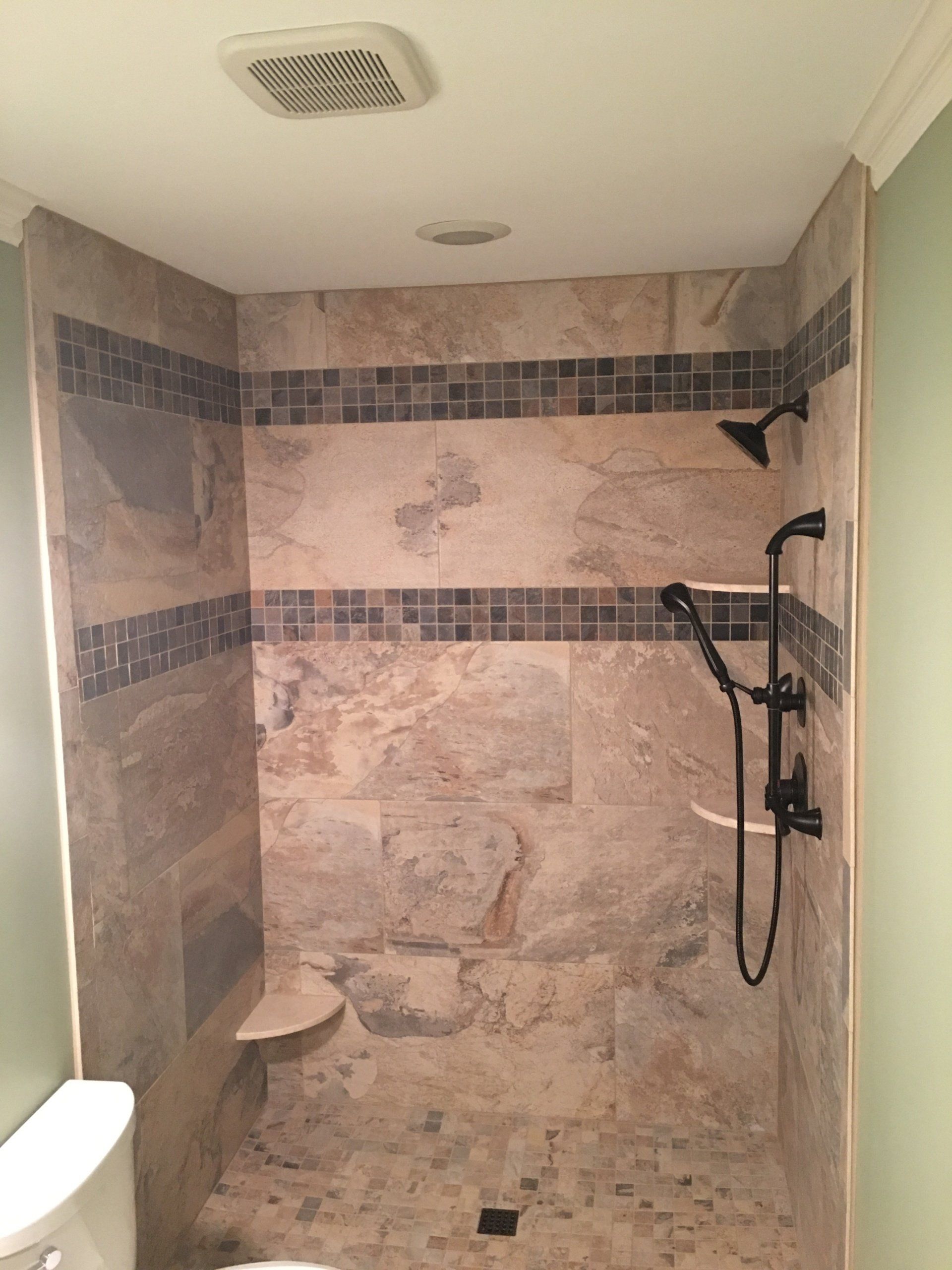 A tiled shower with a built-in bench and multiple showerheads. Beige and brown tones, a dark accent band.