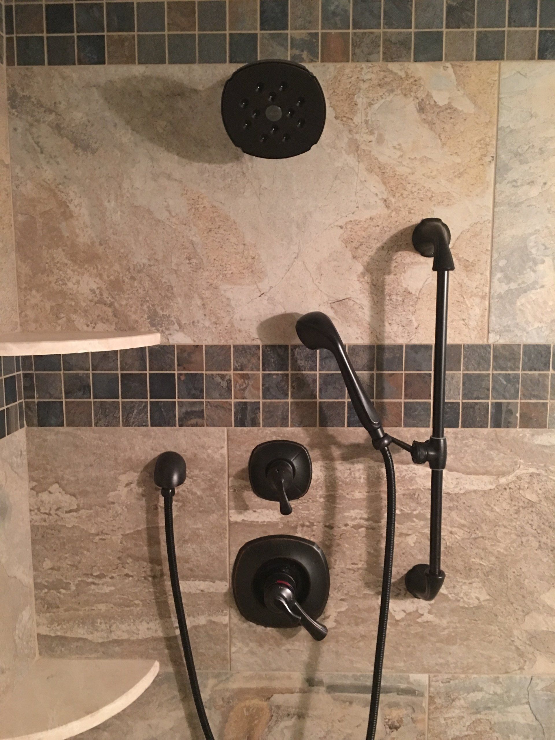 Shower with black fixtures and hand shower against beige and blue tiled wall.