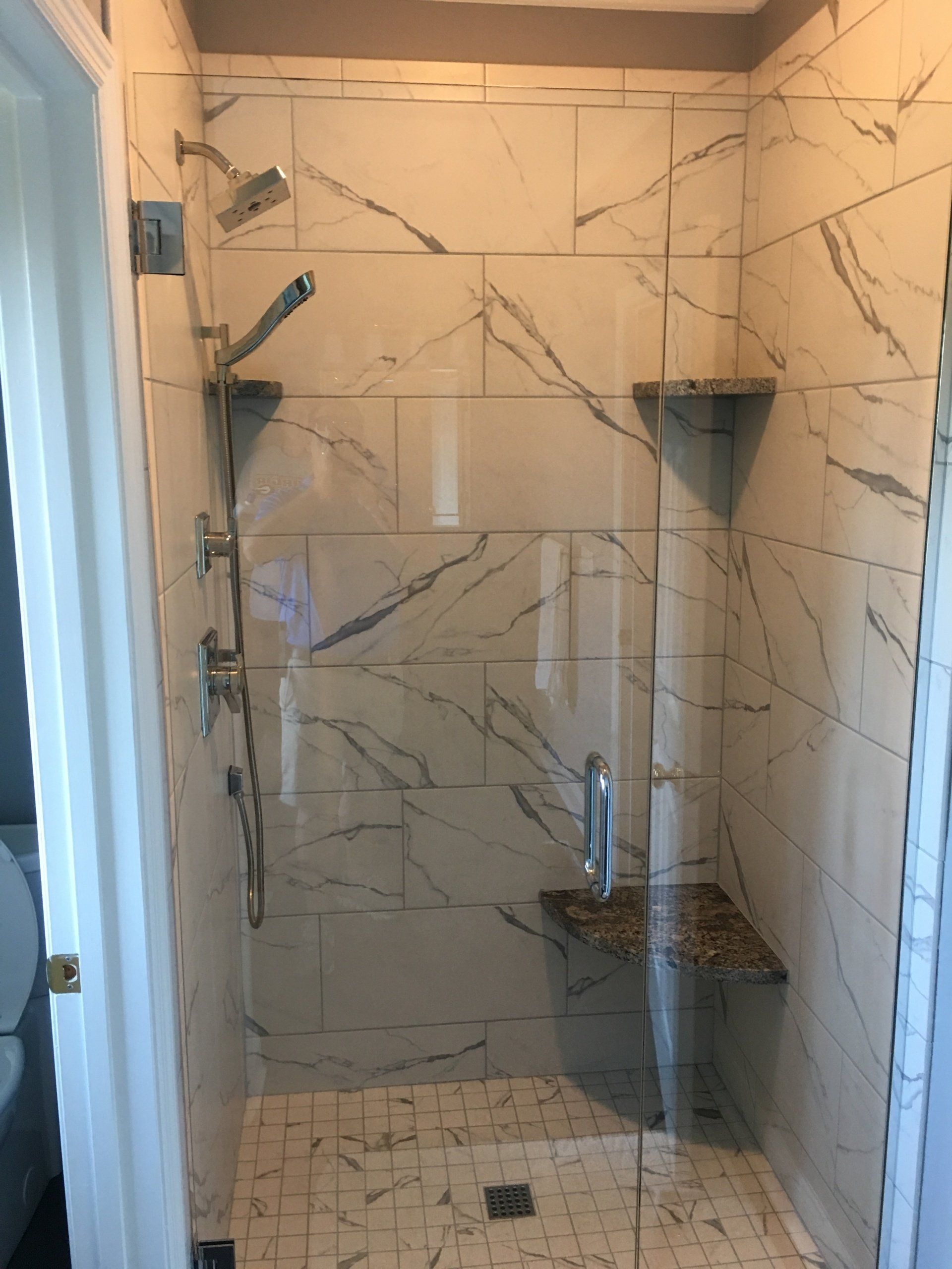 Marble-tiled shower with glass door, built-in seat, and corner shelves. Chrome shower fixtures.
