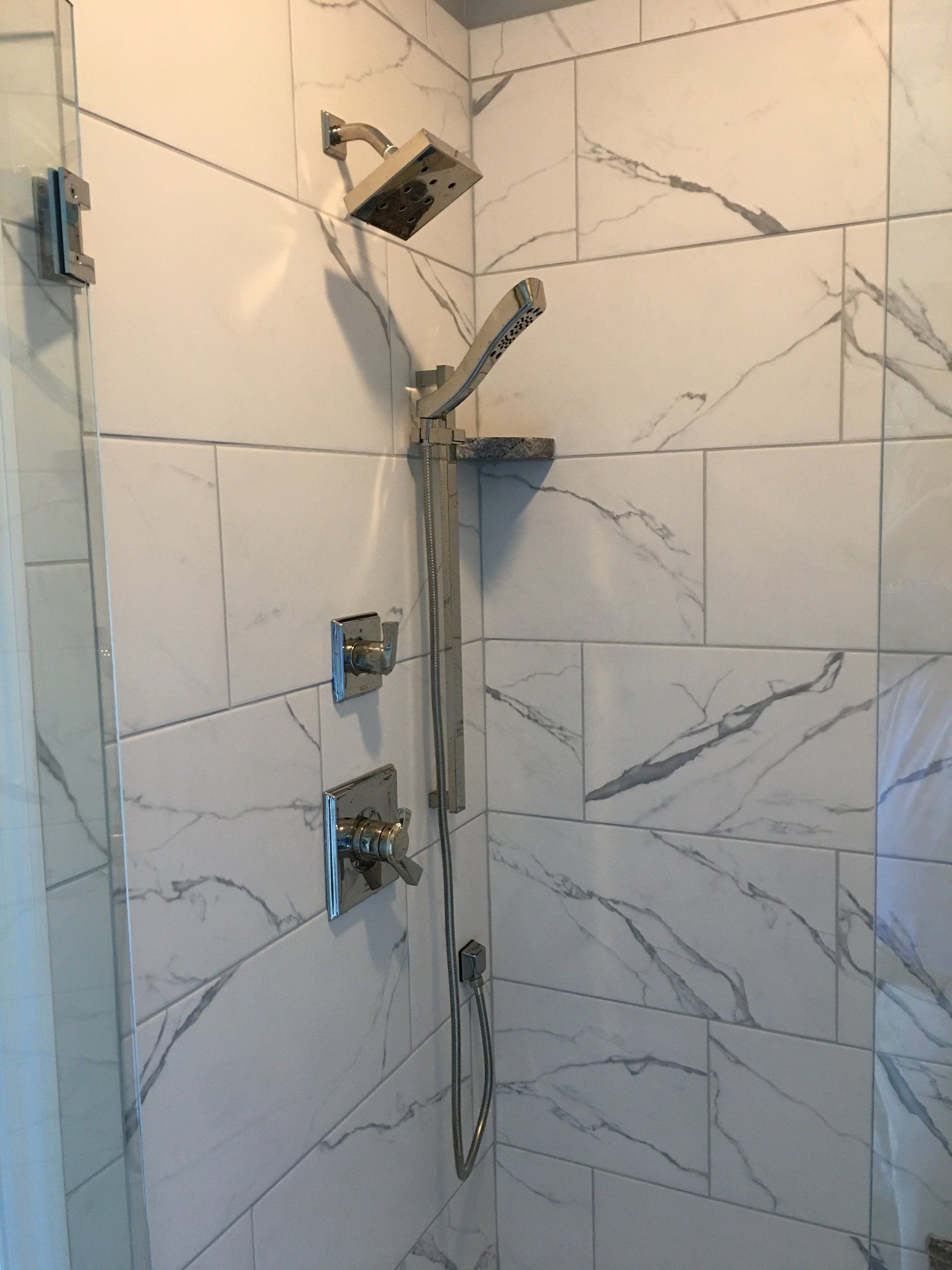 Shower with marble-look tiles, a handheld shower head, and chrome fixtures.
