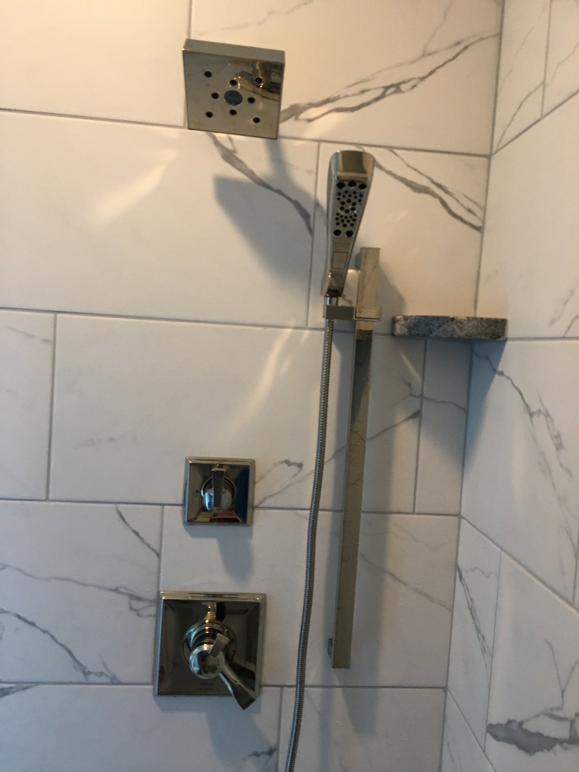 Shower with silver fixtures, white marble-look tile. Top: rain showerhead. Middle: hand shower. Bottom: controls.