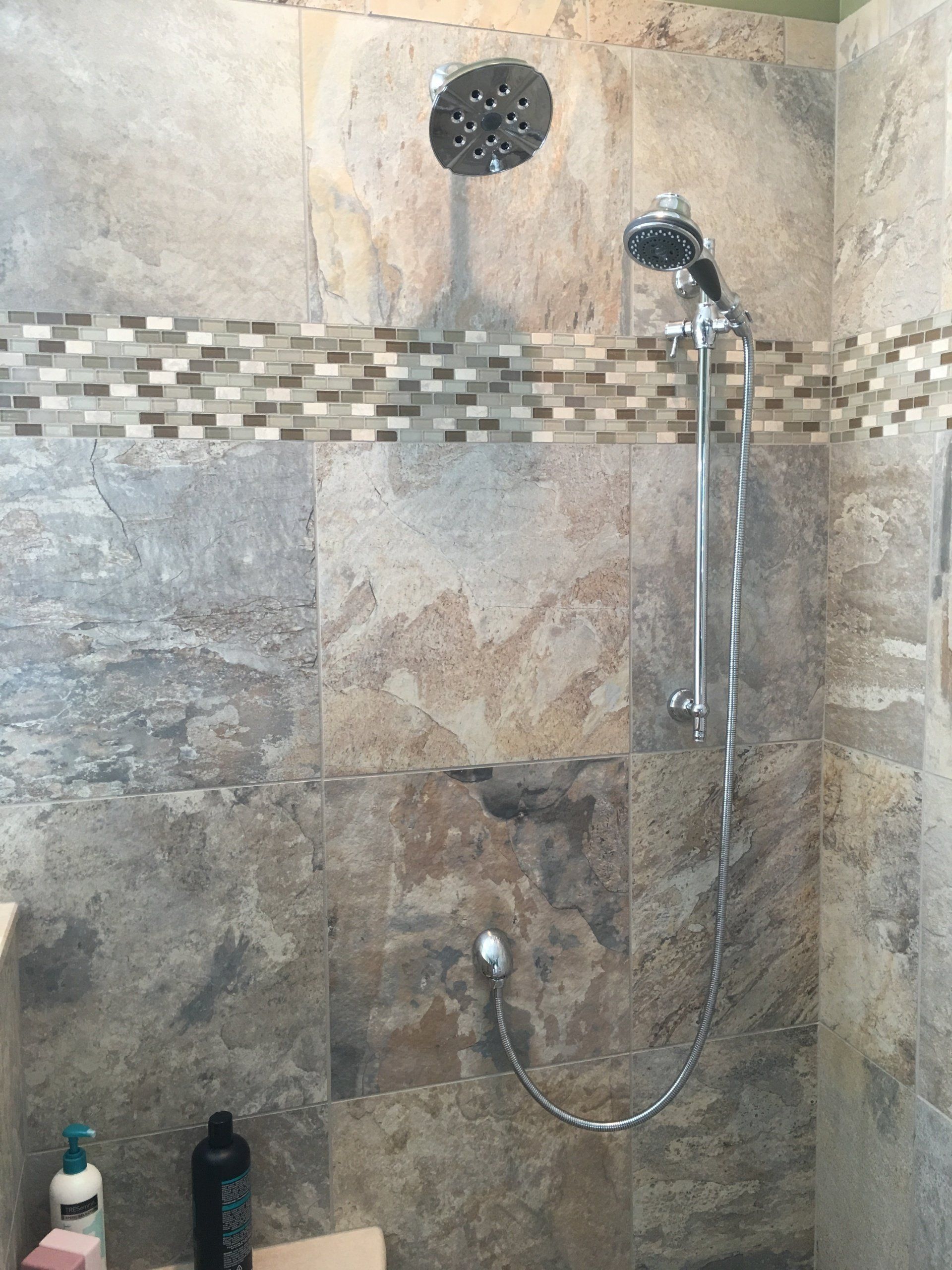 Shower with multi-toned stone tiles, a rain showerhead, and a handheld showerhead, mosaic border.