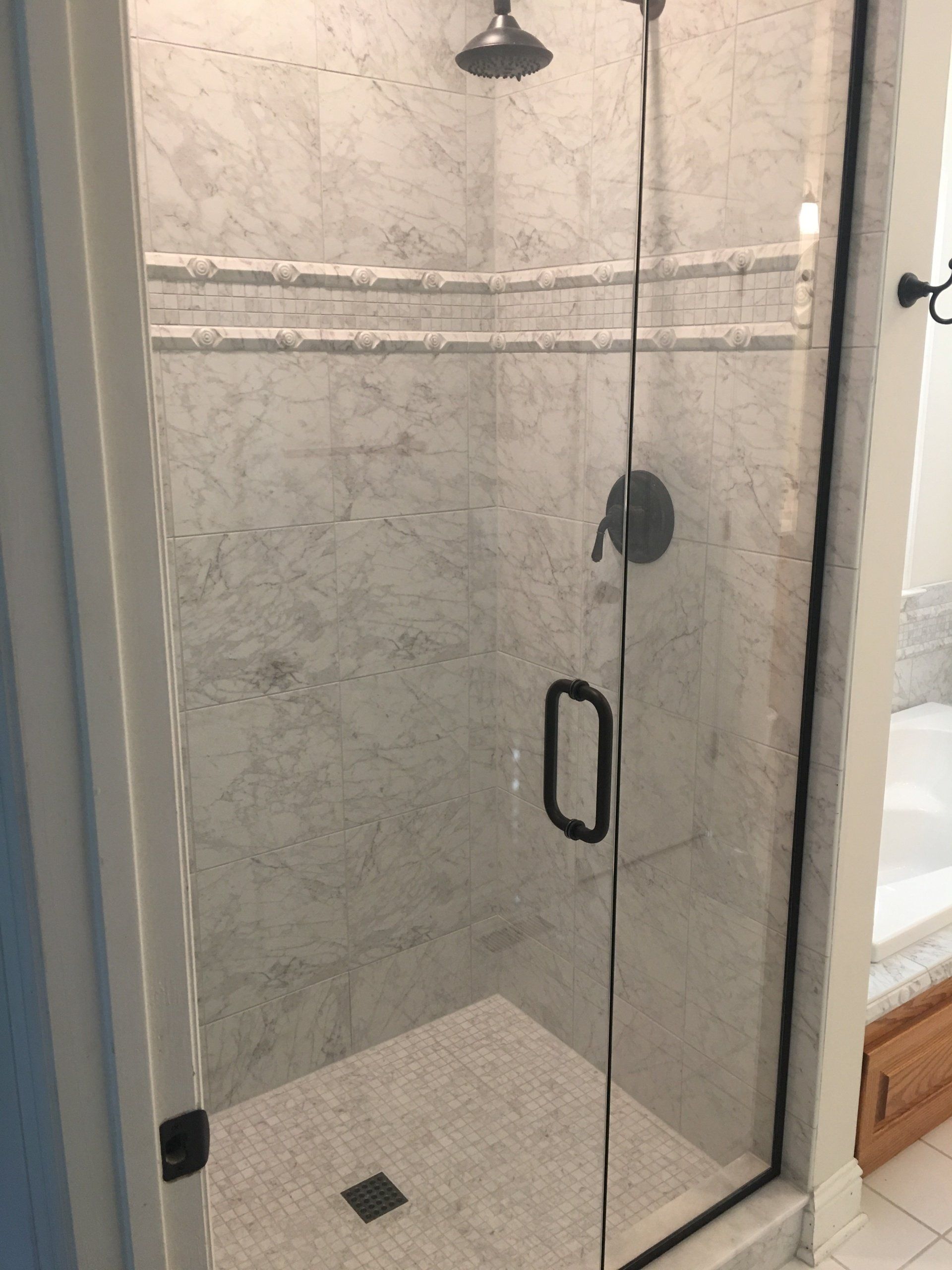 A marble-tiled shower with a glass door, black fixtures, and a white tiled floor.