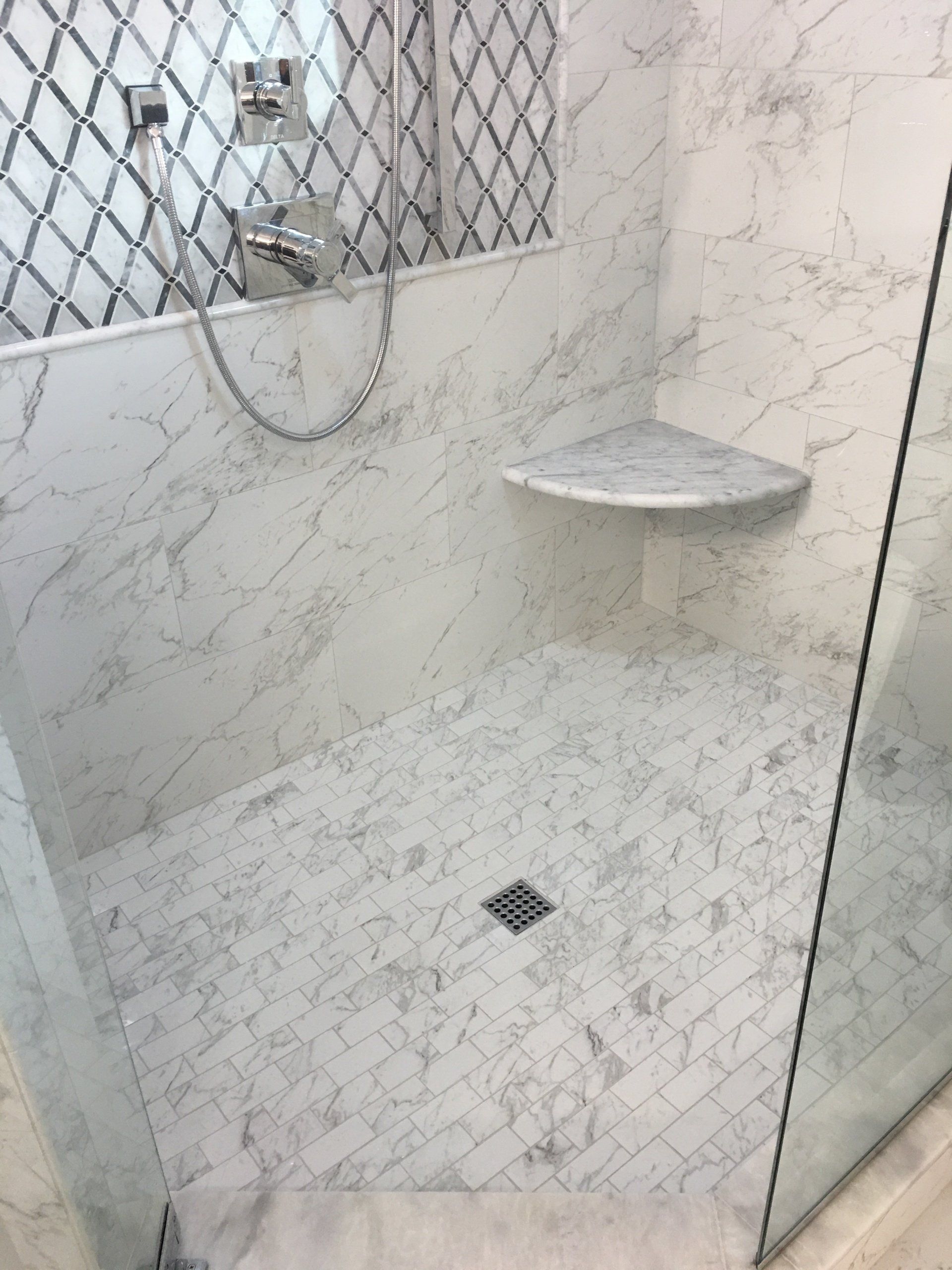 Marble-tiled shower stall with a glass door, corner shelf, and patterned accent wall.