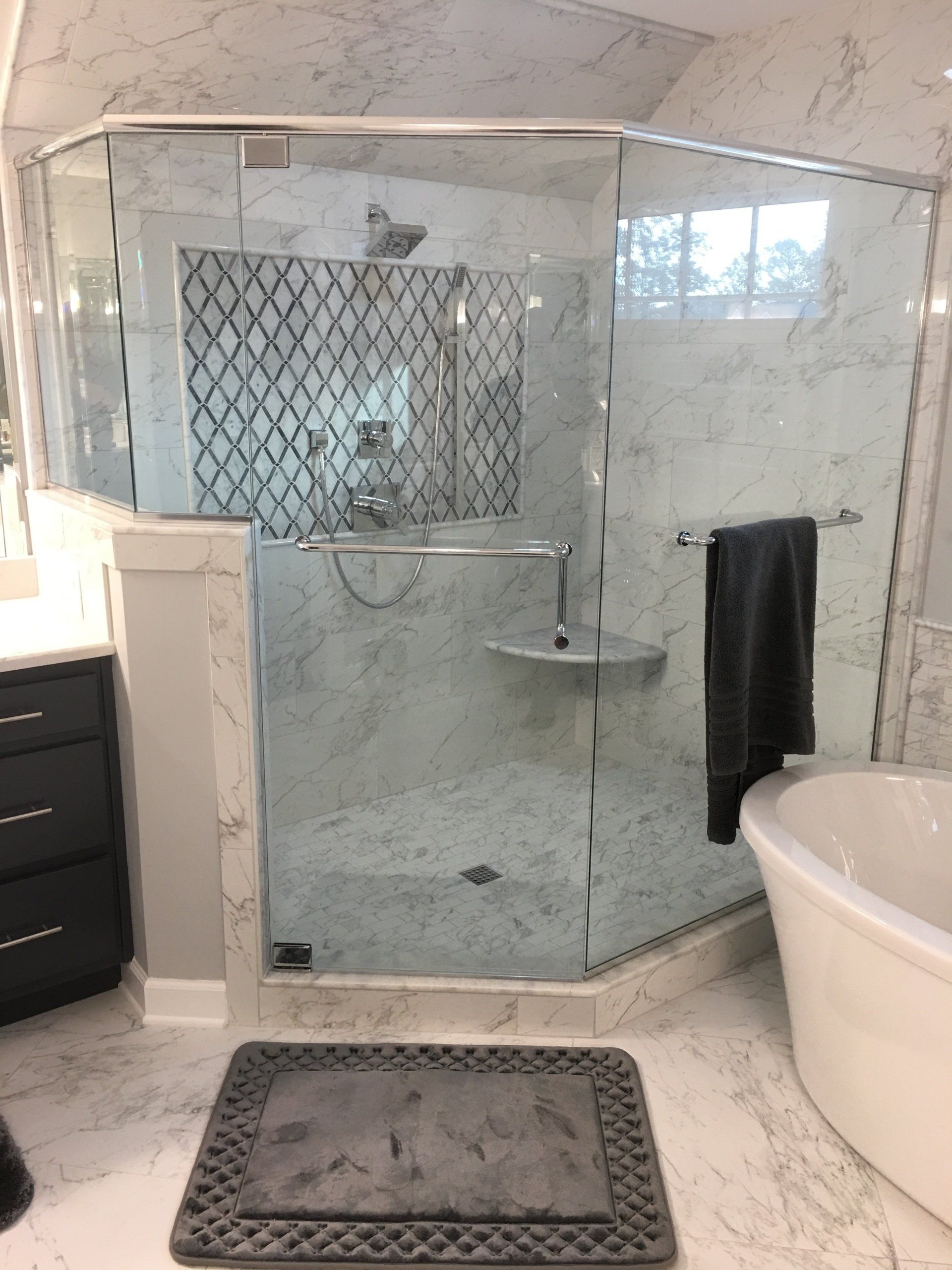 Modern bathroom with marble walls, glass shower, and a freestanding bathtub.