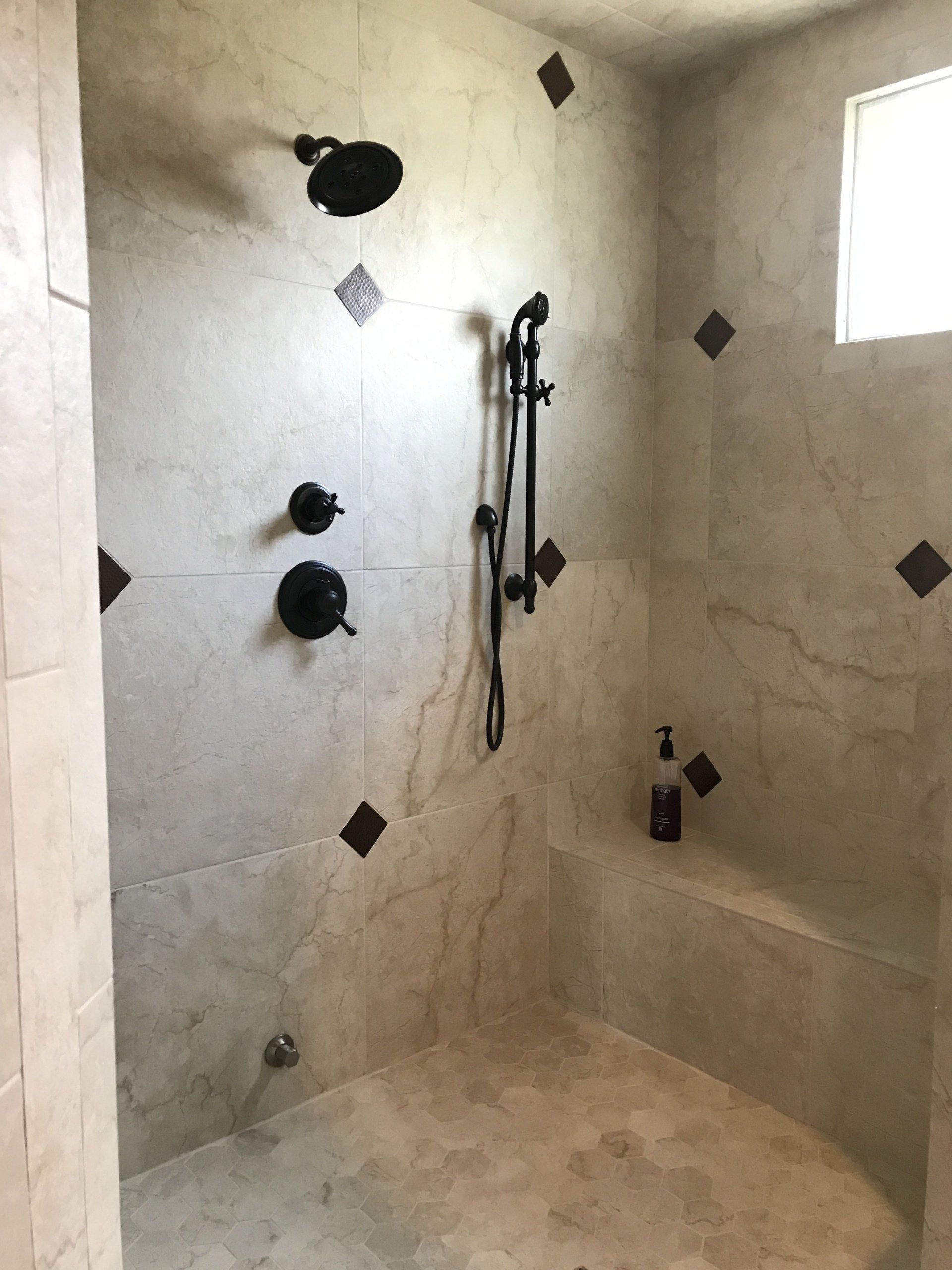 Bathroom shower with light tile, dark fixtures, and a built-in bench.