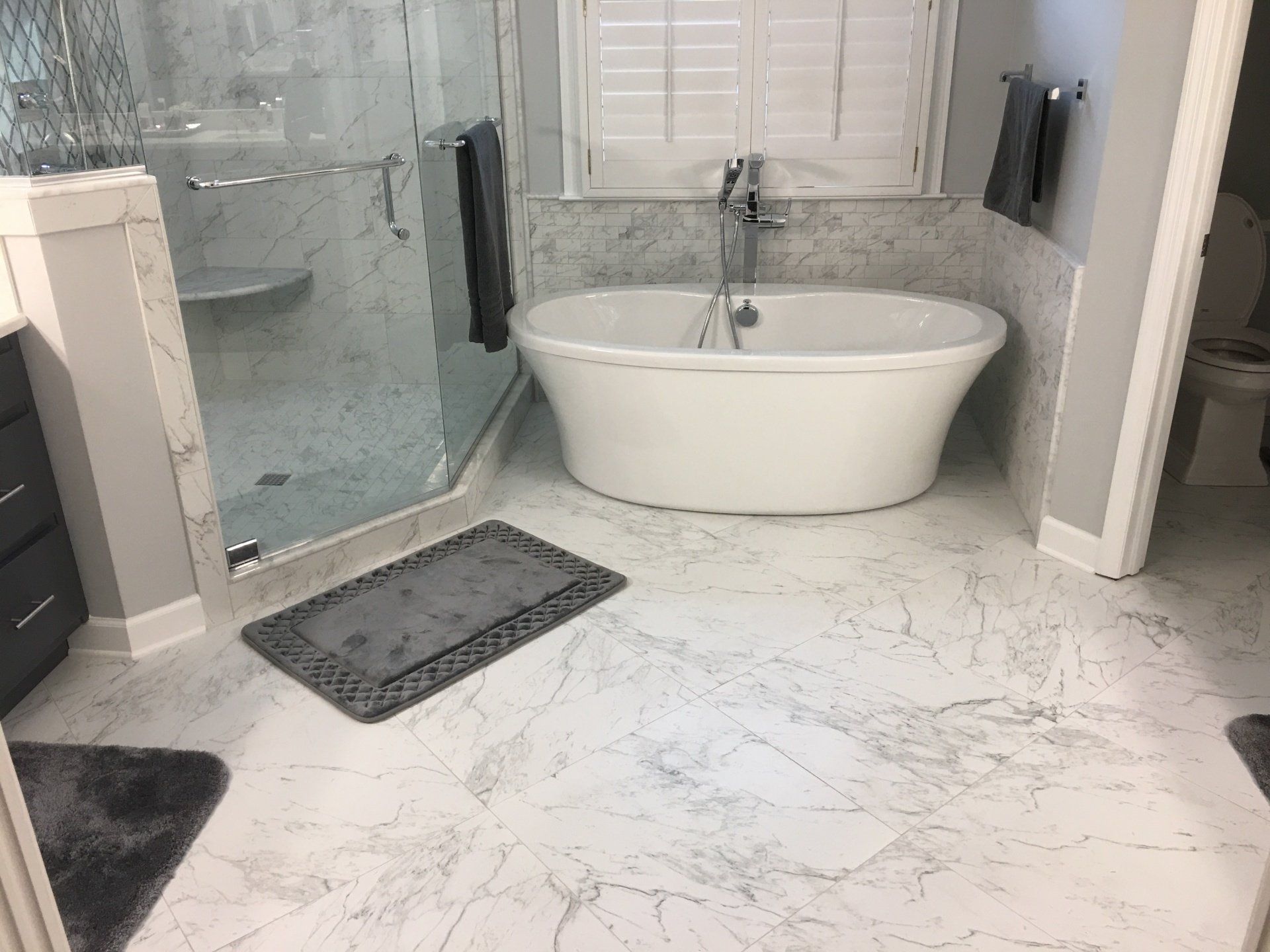 Elegant bathroom with a white tub, glass shower, and marble-patterned flooring.