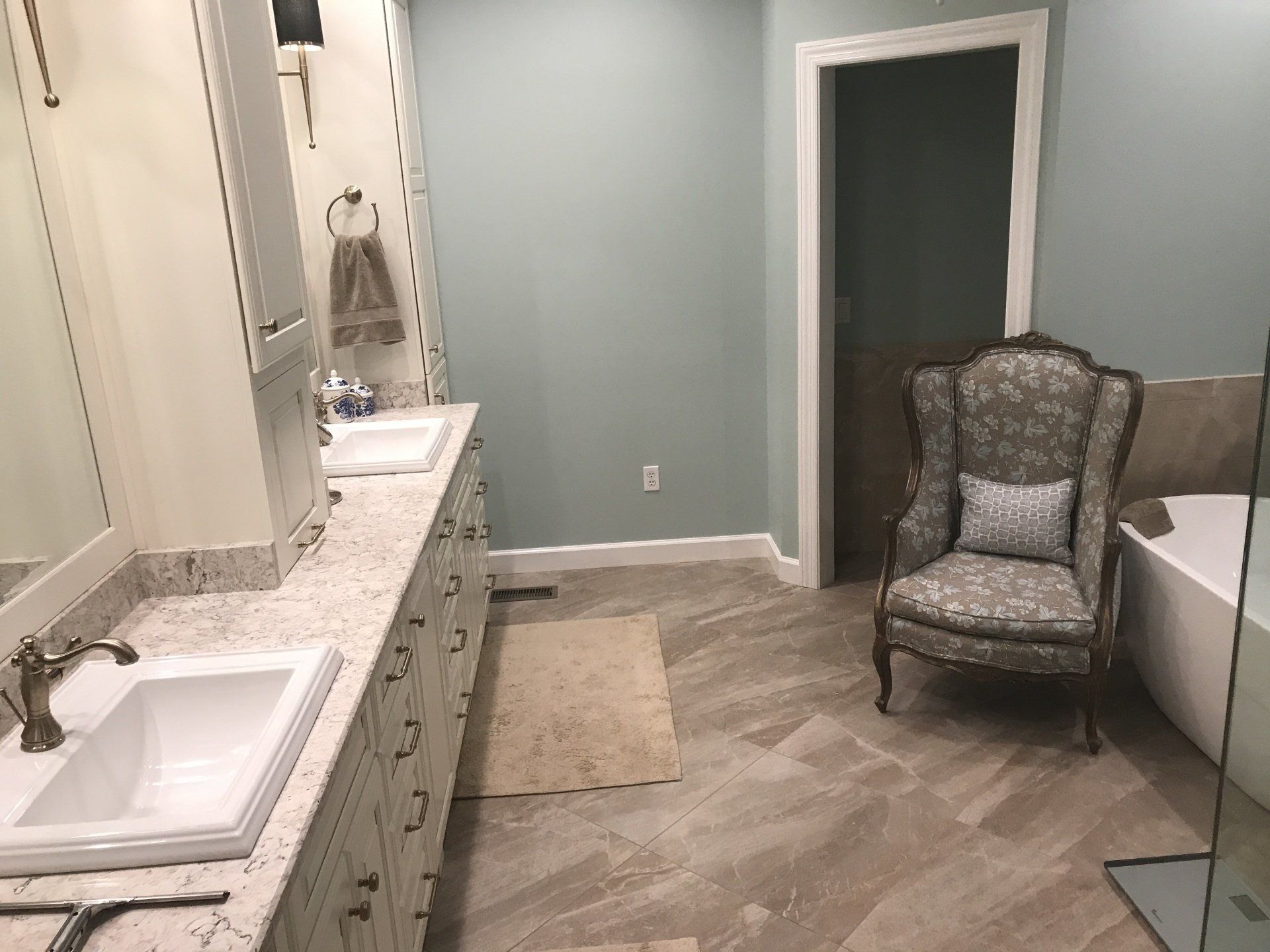 Bathroom with vanity, chair, bathtub, and pale blue walls.