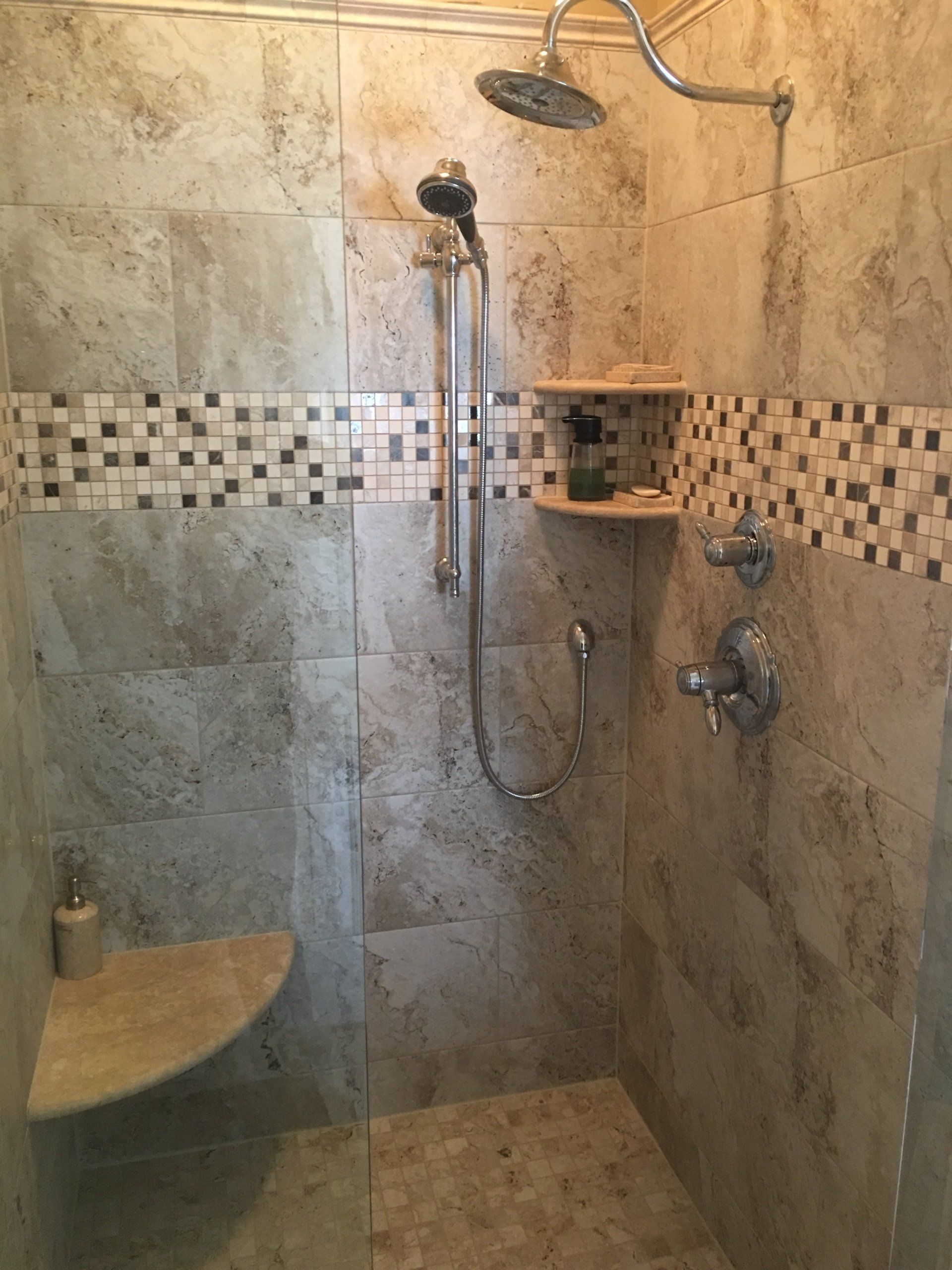 Shower with beige tile, mosaic border, two shelves, and silver fixtures.