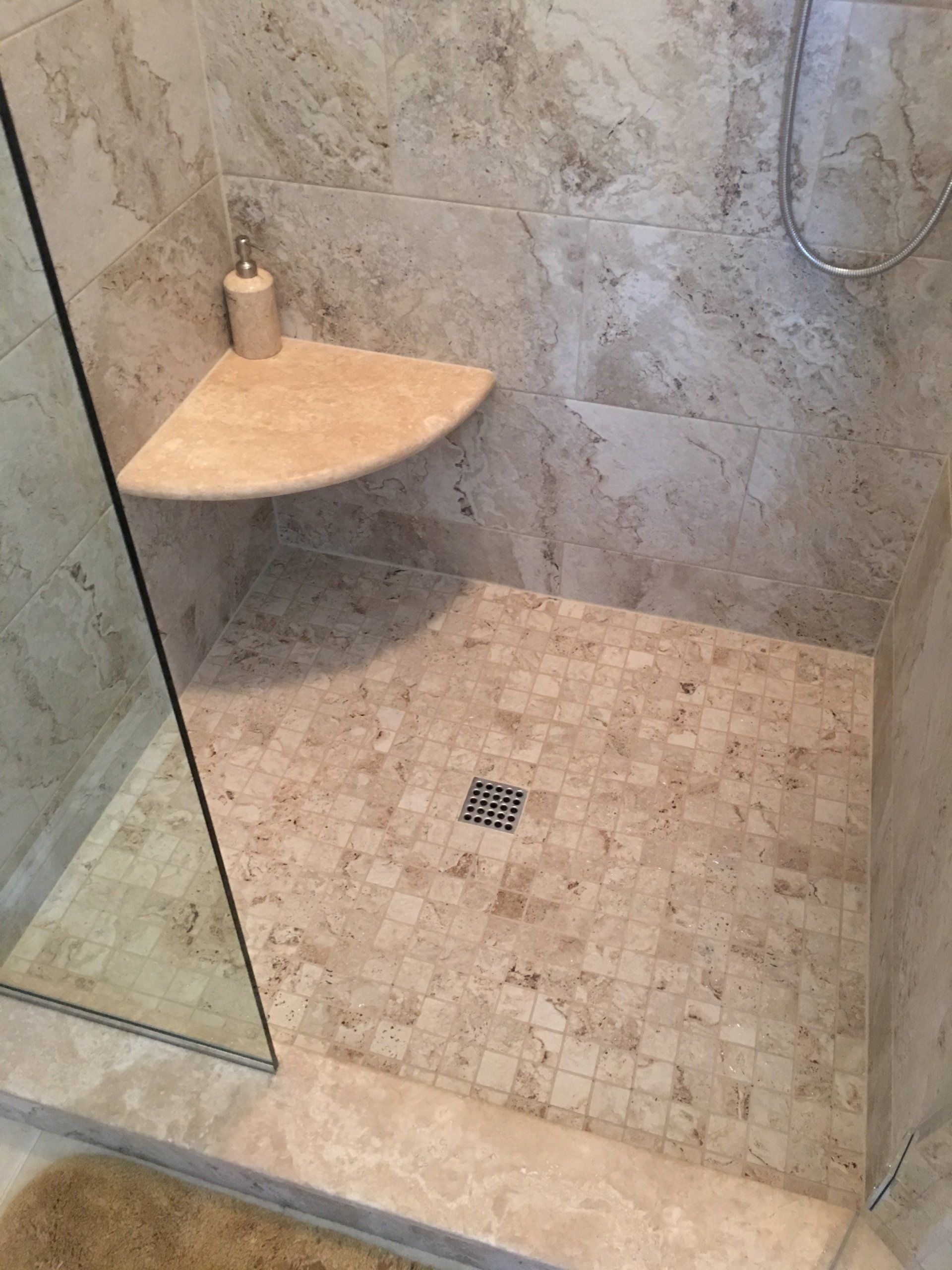 Shower with beige stone tile, a corner shelf, and glass door.