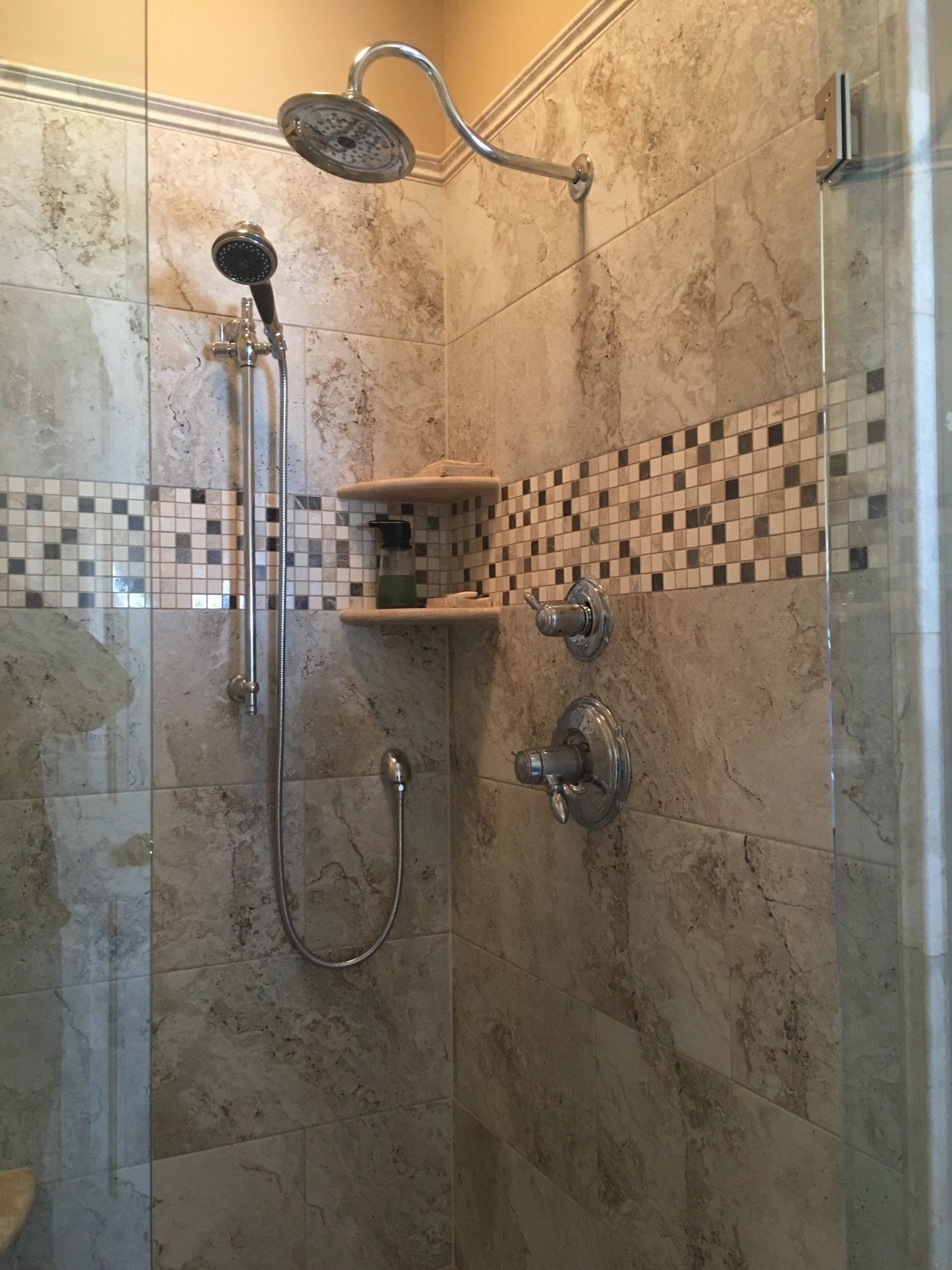 Shower with stone tiles, mosaic border, two showerheads, and built-in shelf.