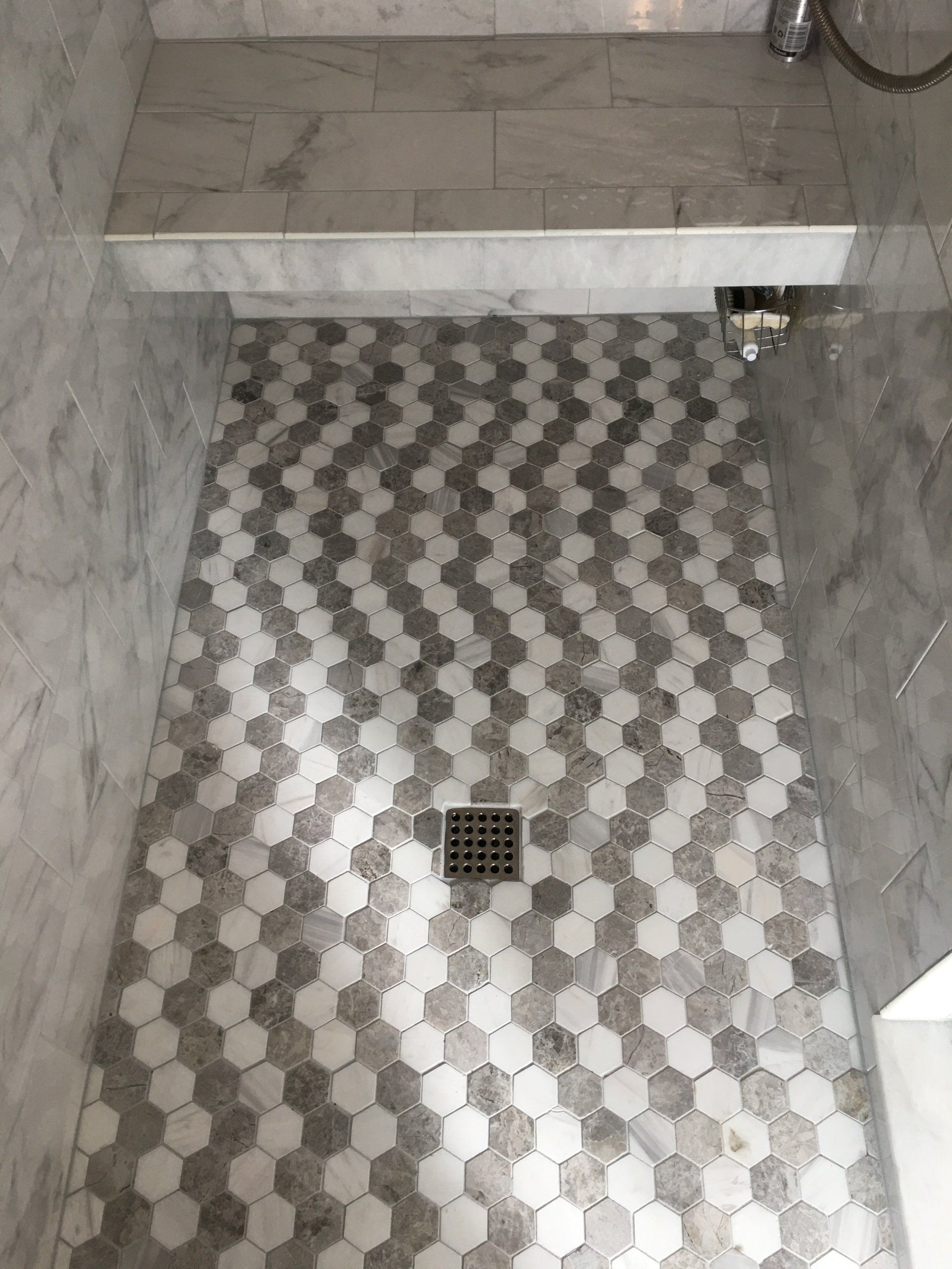 Shower floor with gray and white hexagonal tiles and a metal drain.