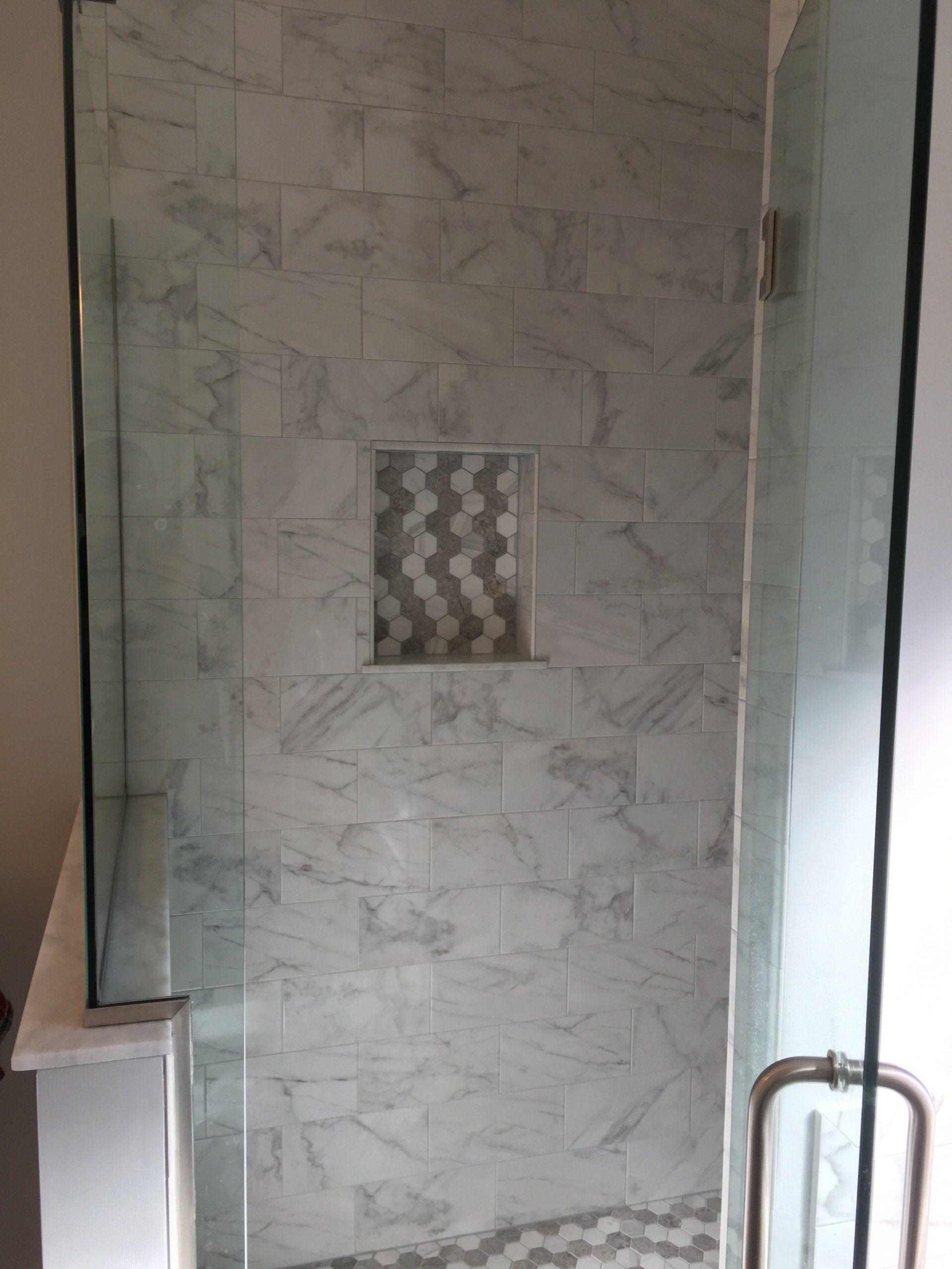 Shower with glass doors, marble tile walls, and a hexagonal tile inset.