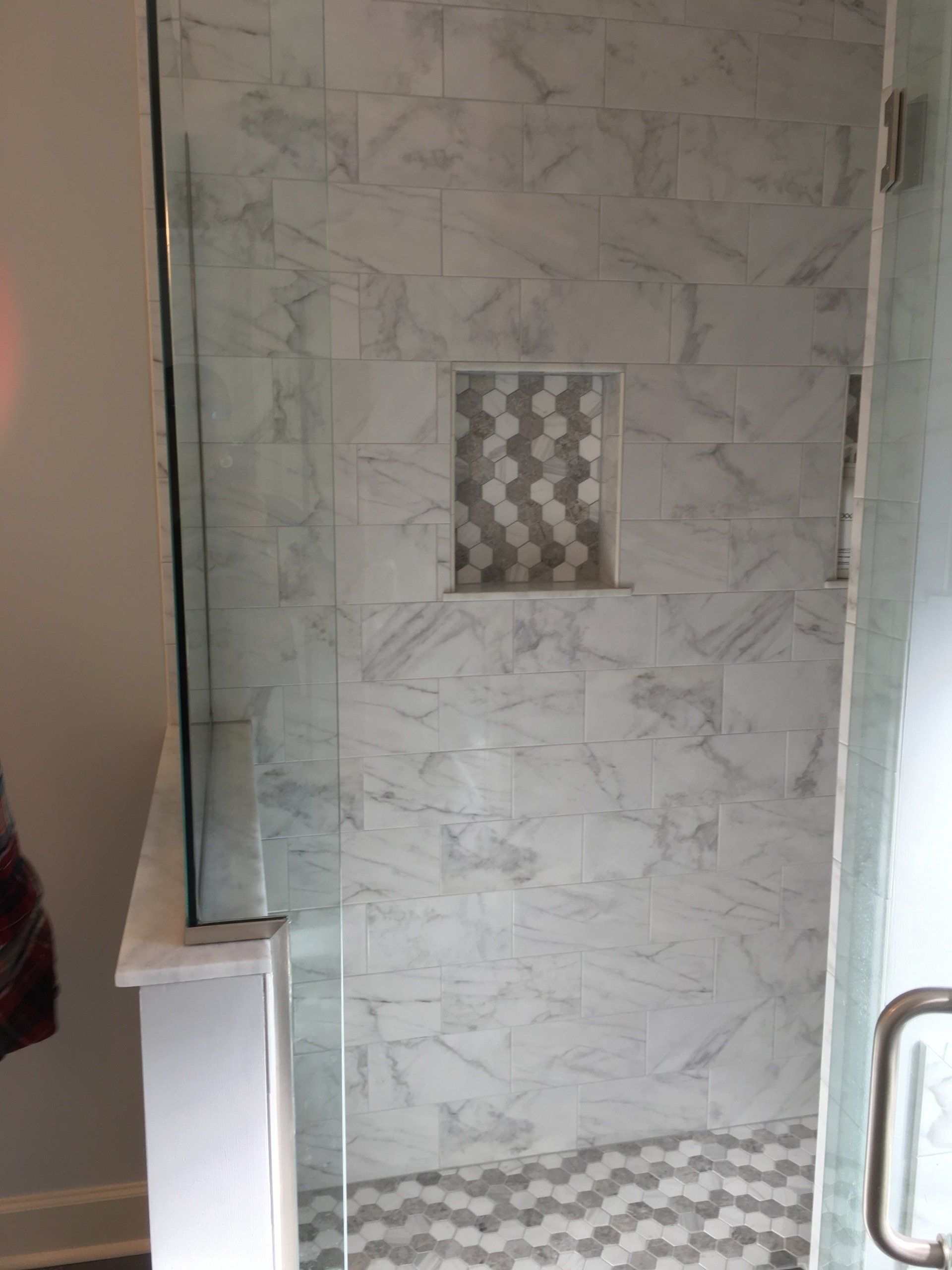 Shower with marble-look tile, glass door, and built-in shelf with patterned tile.