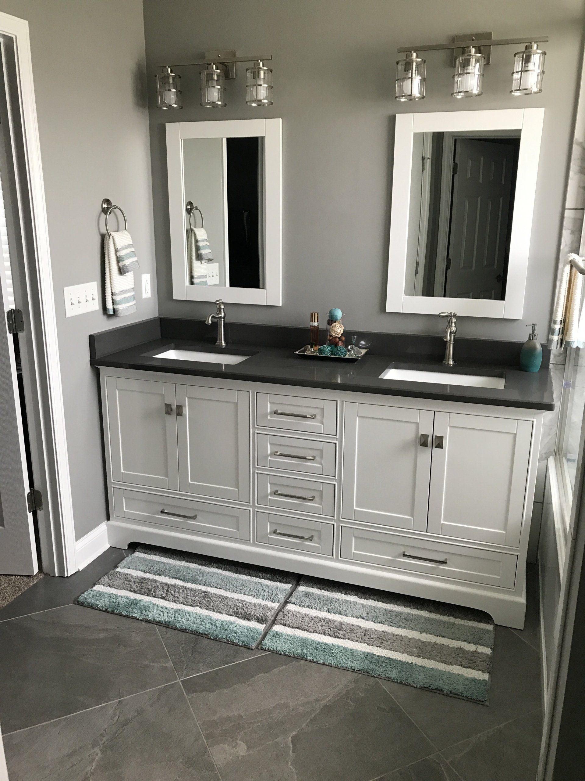 Bathroom with gray walls, white double vanity, gray countertop, and striped rug.
