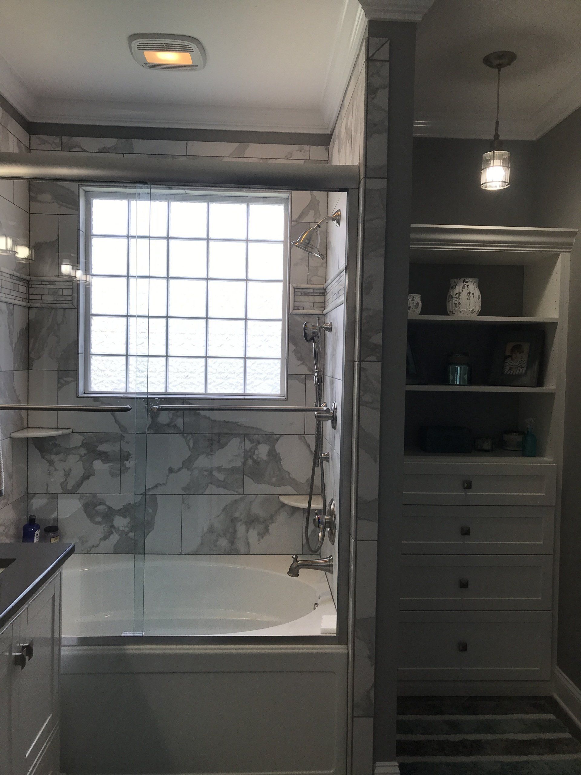 Bathroom with marble tile, glass shower door, built-in shelves, and a pendant light.