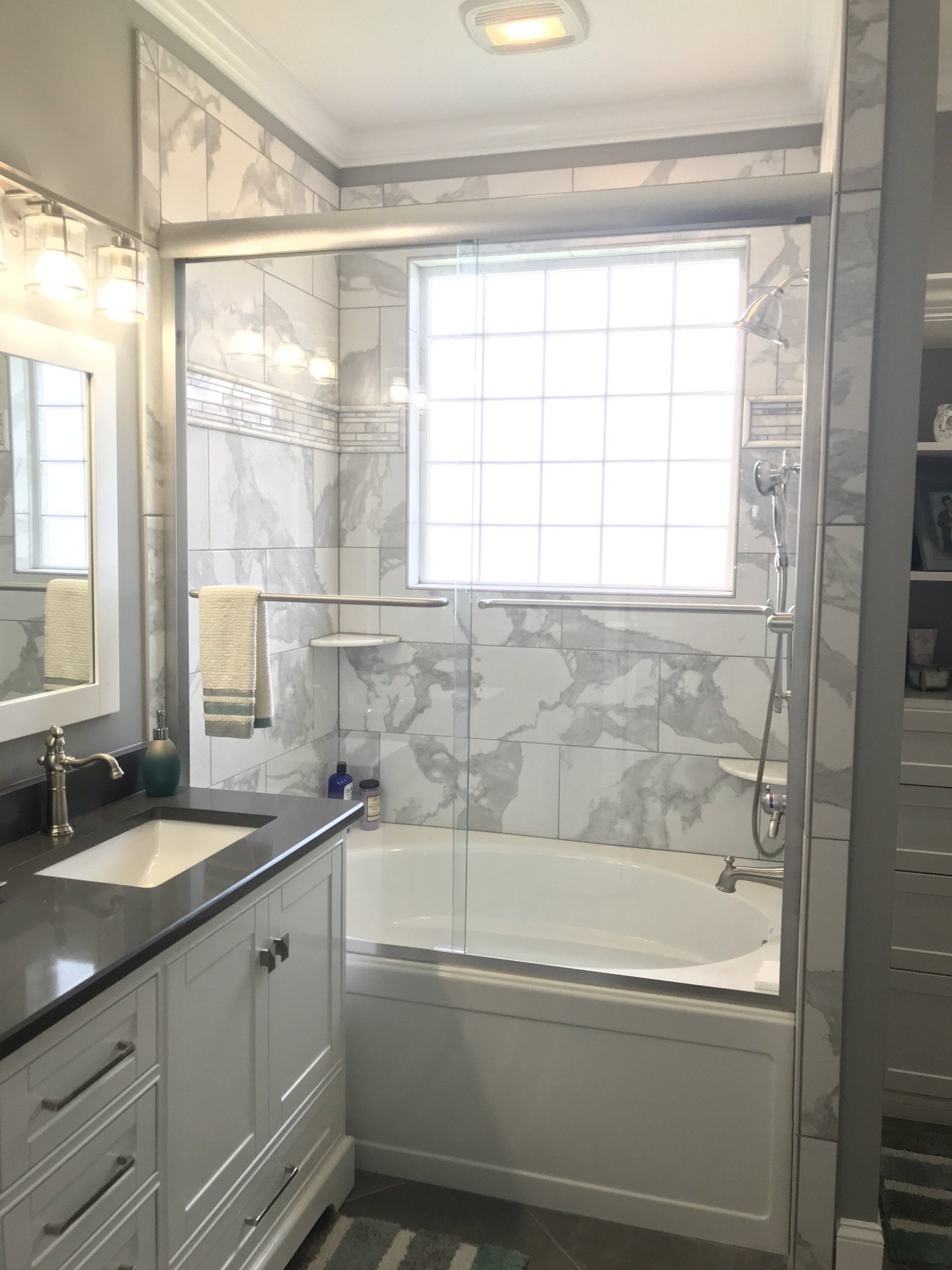 Bathroom with white vanity, bathtub, and marble-like tiled walls. A window is centered above the tub.