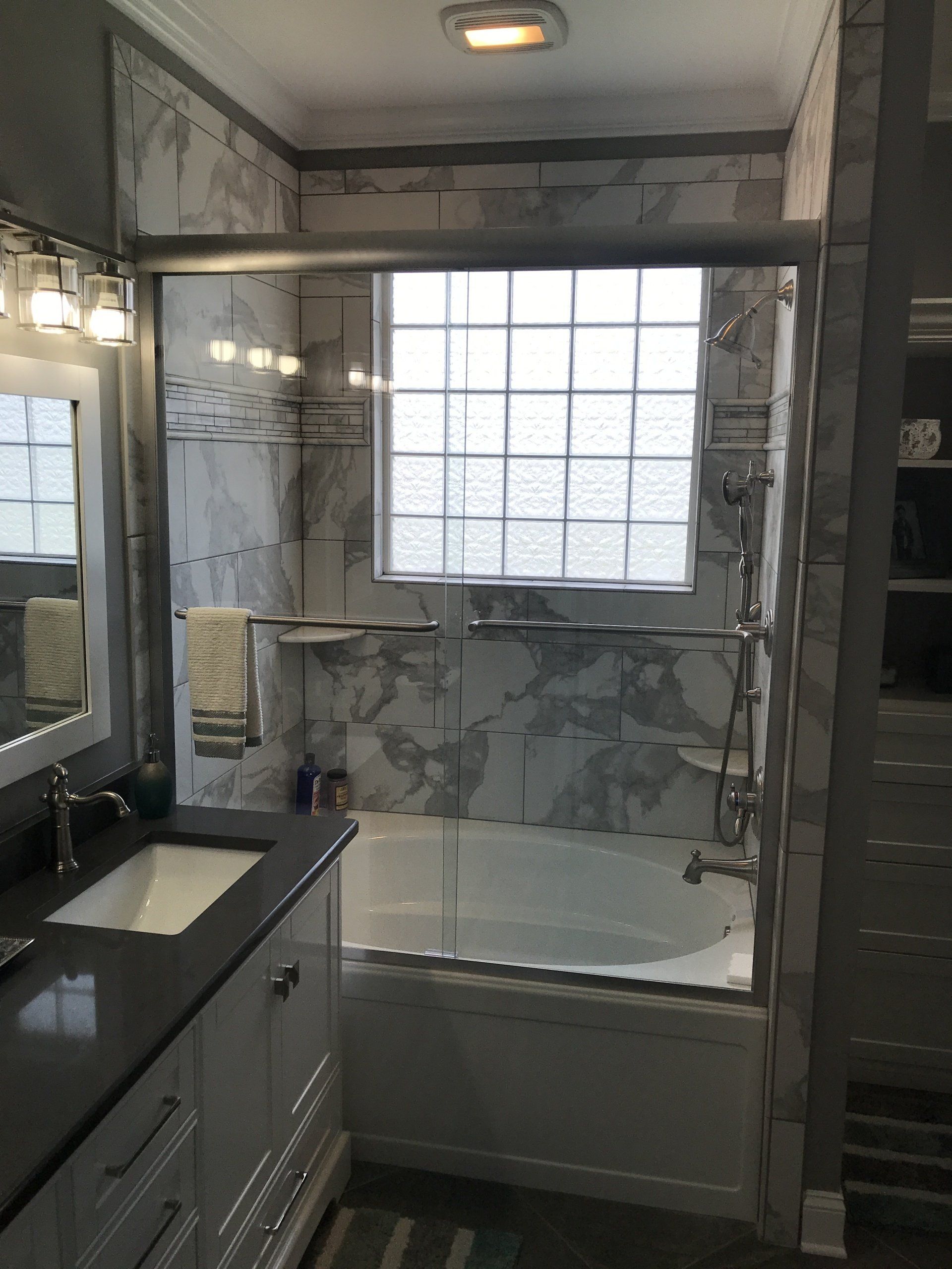 Bathroom with glass shower doors, marble tile, white vanity, glass block window.