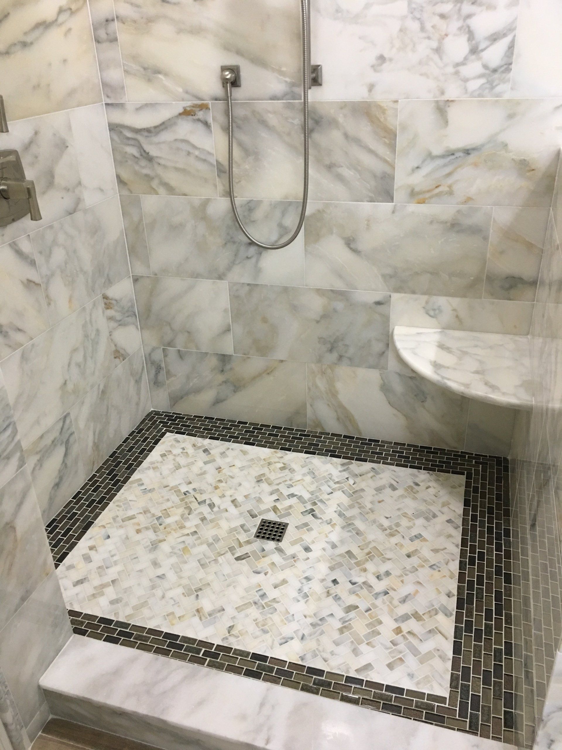 Marble-tiled shower stall with a mosaic floor and a built-in soap niche.