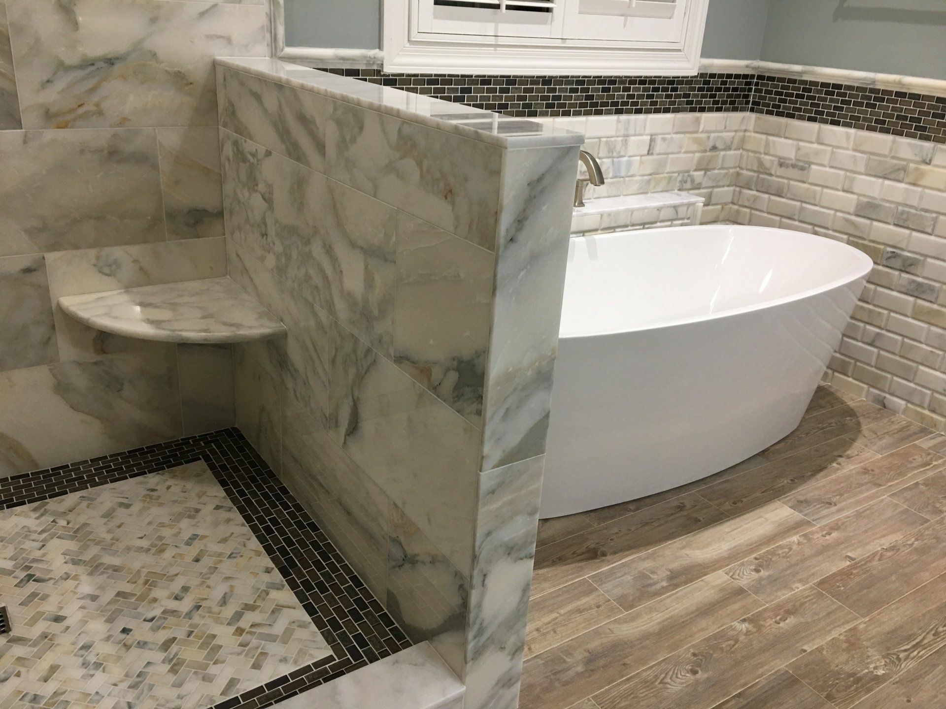 Bathroom with marble shower, white tub, wood-look floor.
