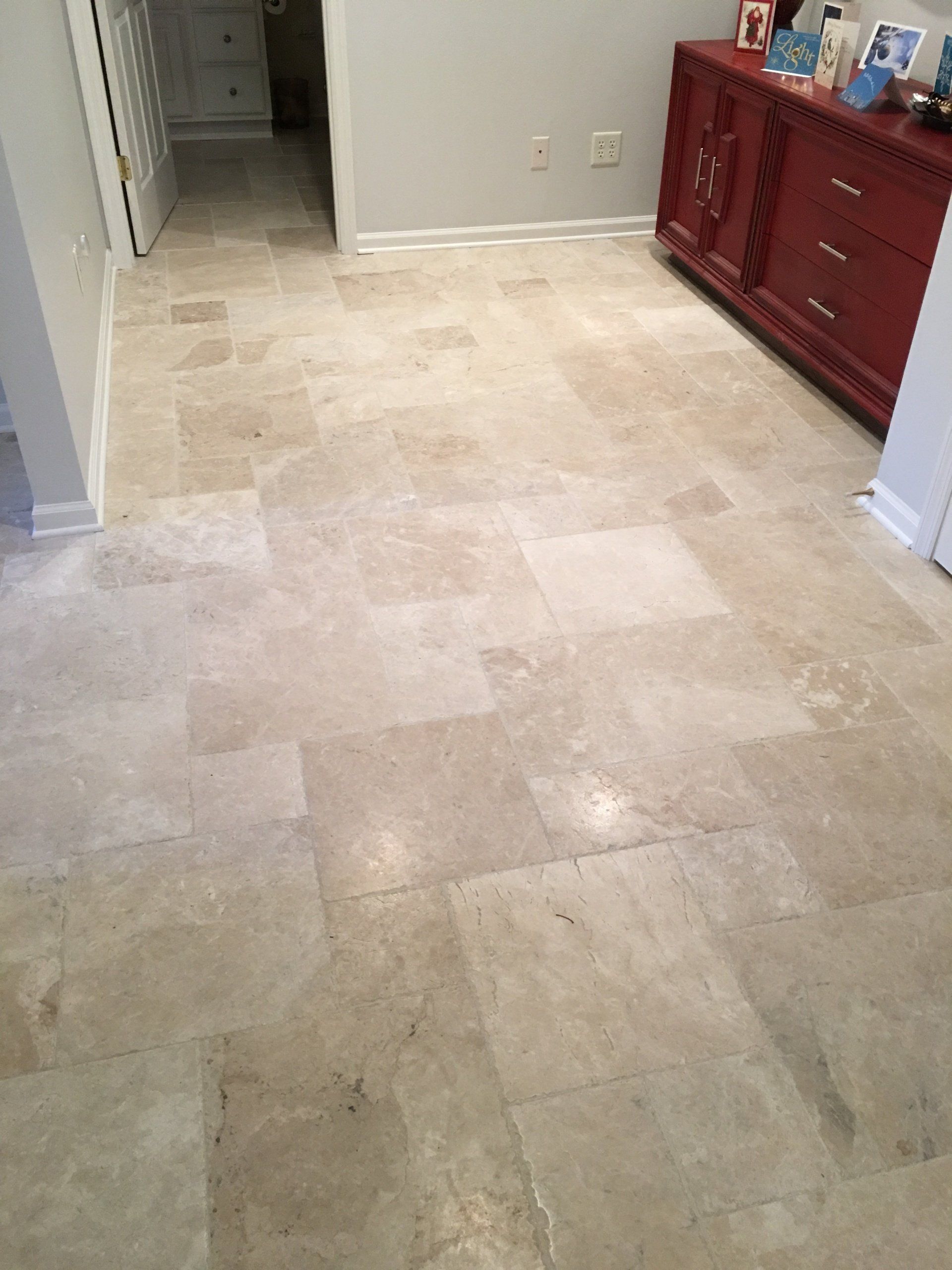 Tan stone tile floor in a room, with a red dresser and a doorway visible.