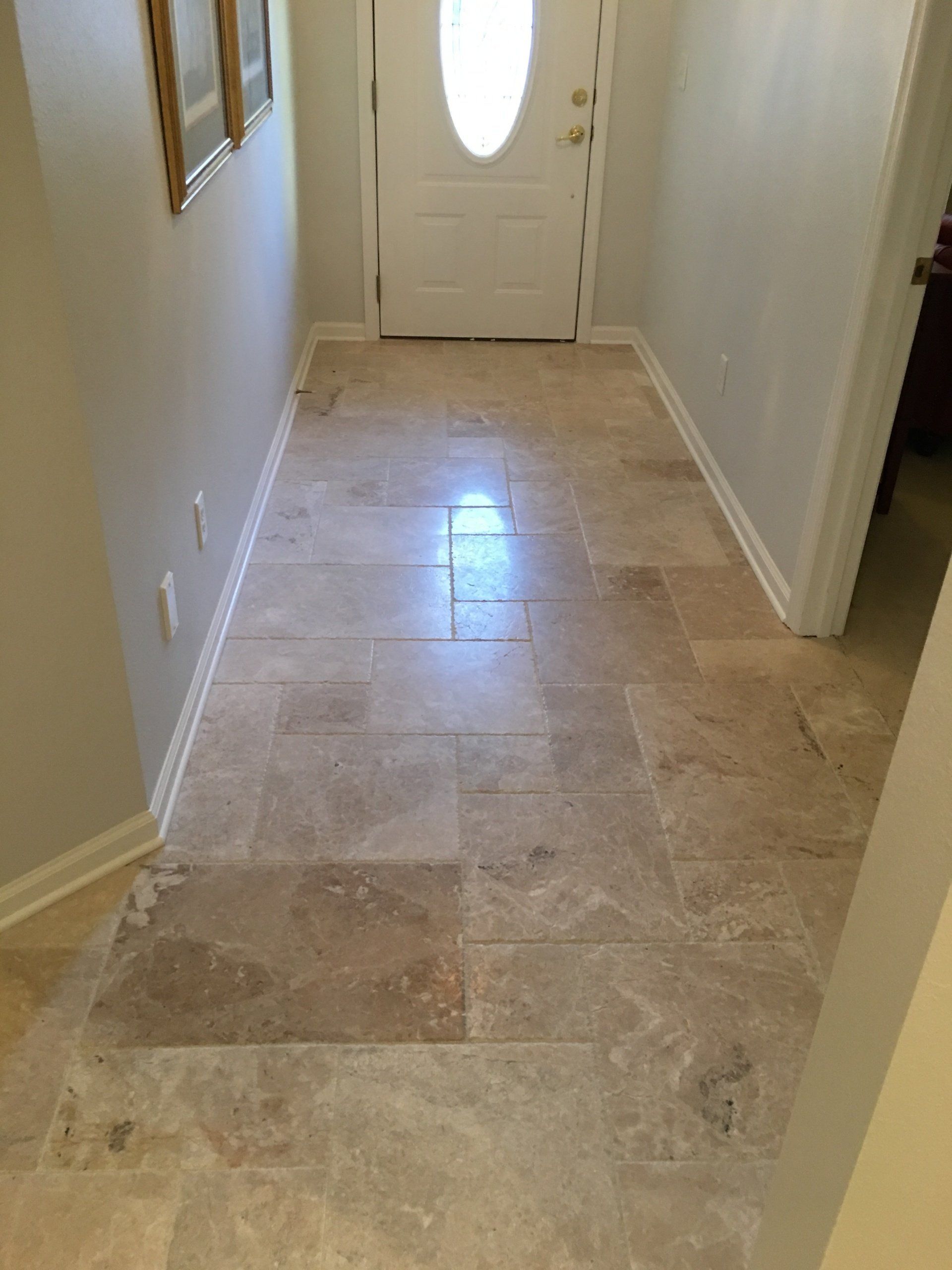 Hallway with tan stone tile flooring, a white front door, and neutral-colored walls.