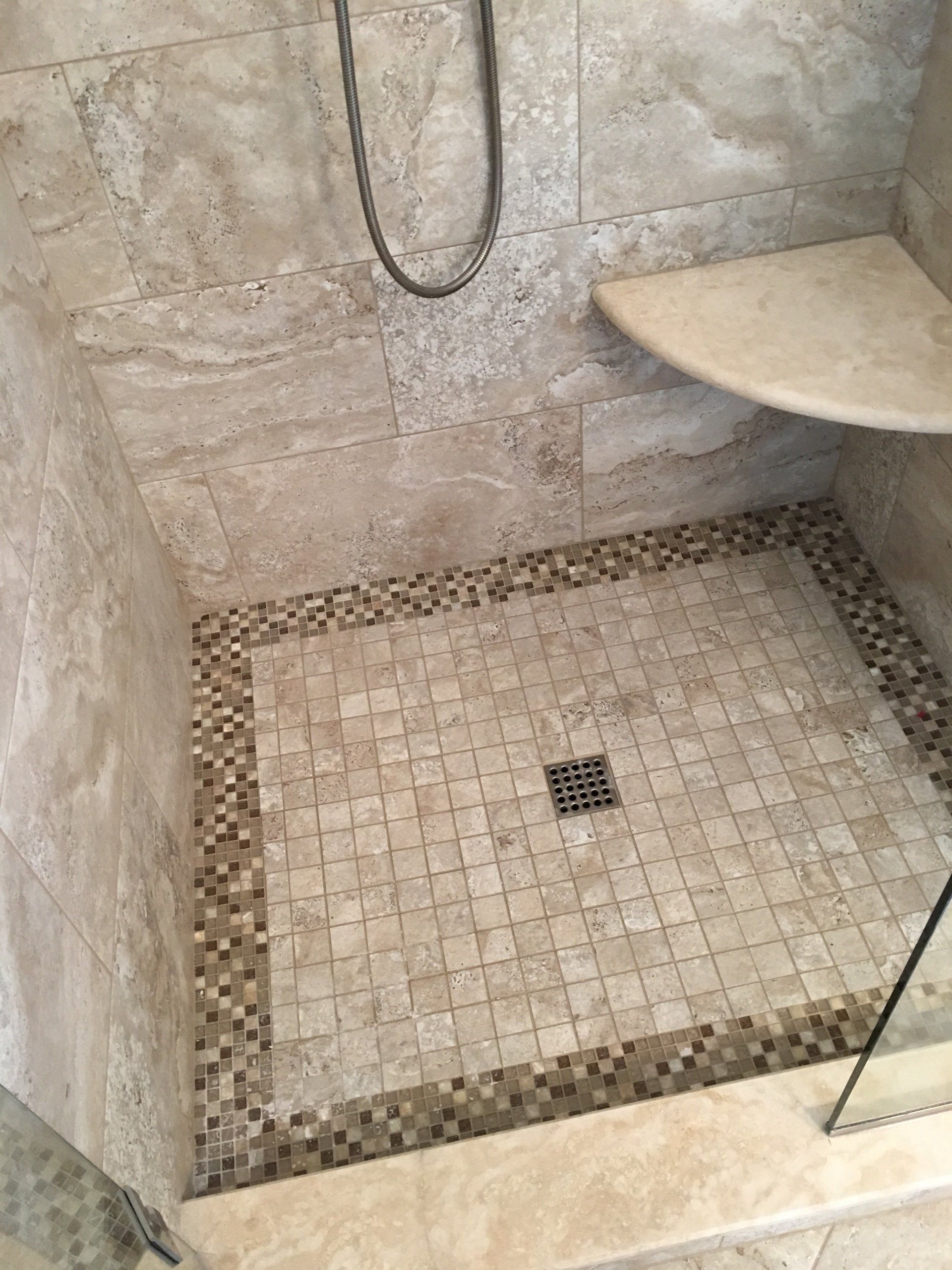 Shower stall with beige tile and mosaic border, corner seat, drain.