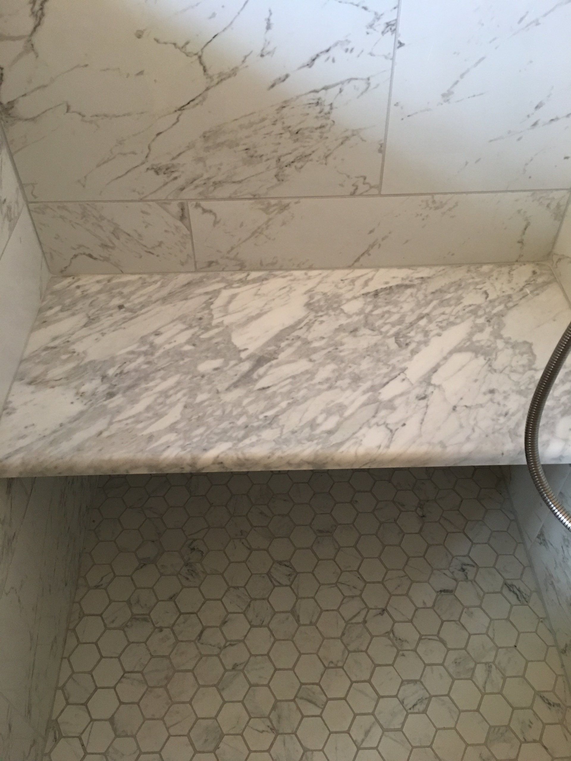 Marble shower with built-in bench, white marble tile walls and hexagon floor tiles.