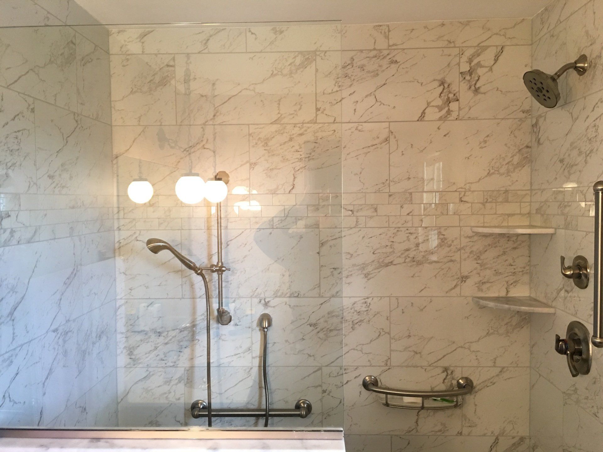 Marble-tiled shower with grab bars, handheld shower, and shelves for easy access.
