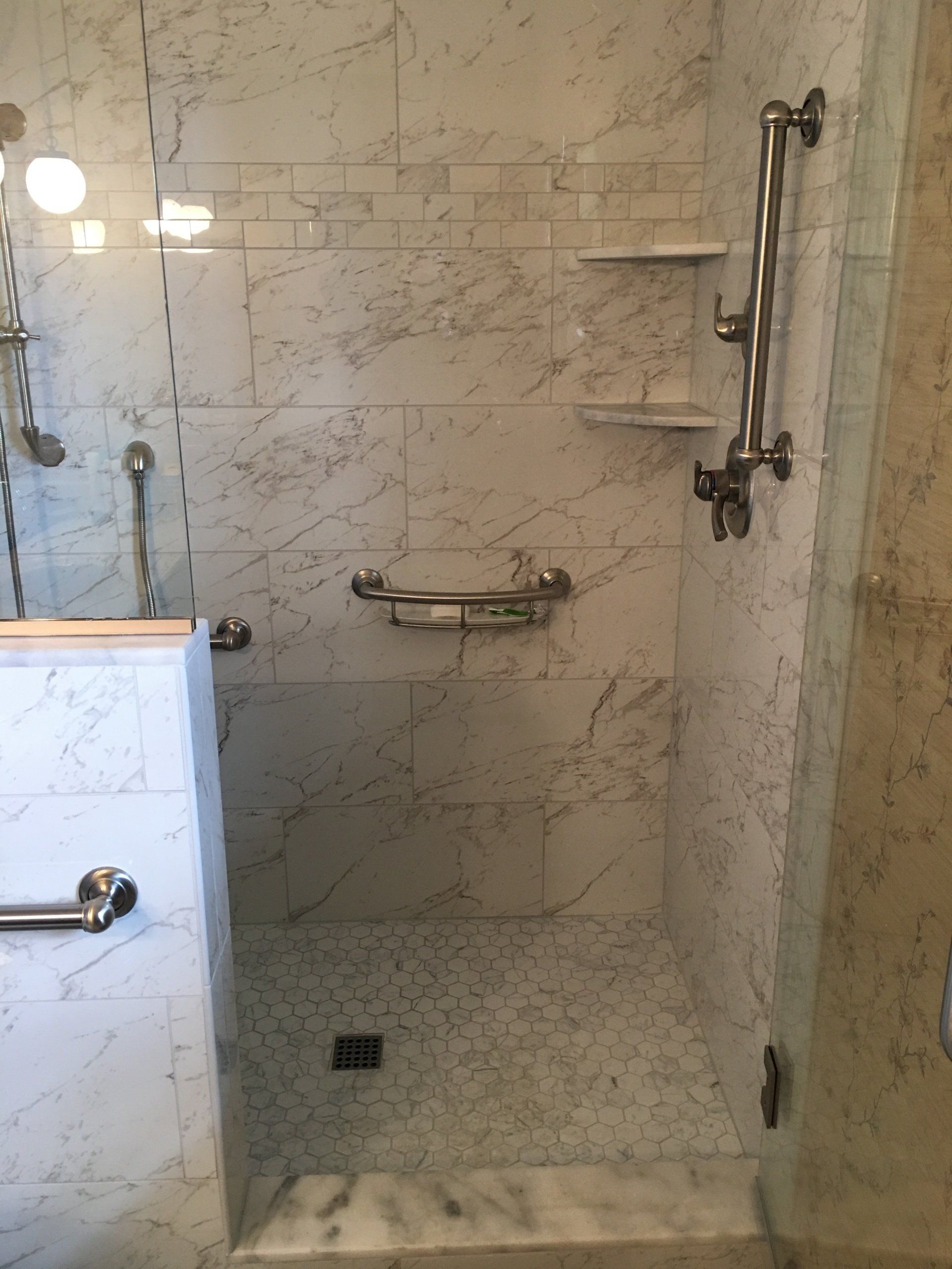 Marble-tiled accessible shower with grab bars, shelves, and a hand shower.