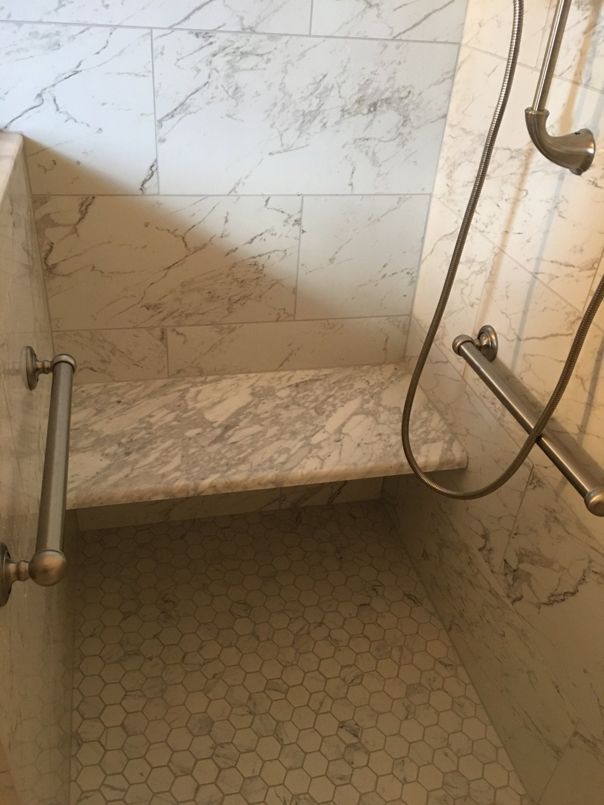 Marble shower stall with bench and grab bars.