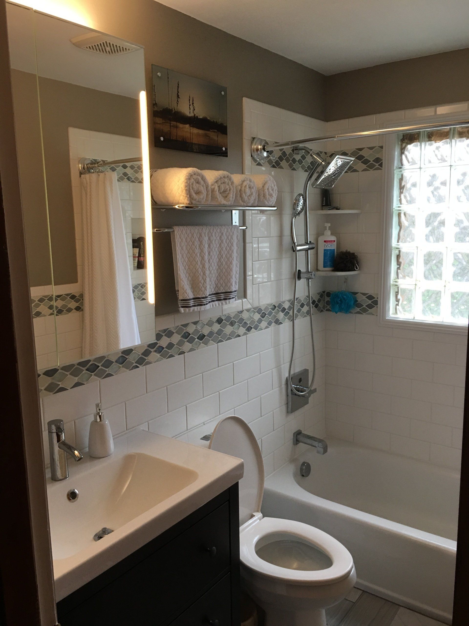 Small bathroom with a white tiled shower, toilet, and sink. Towels hang above the toilet.