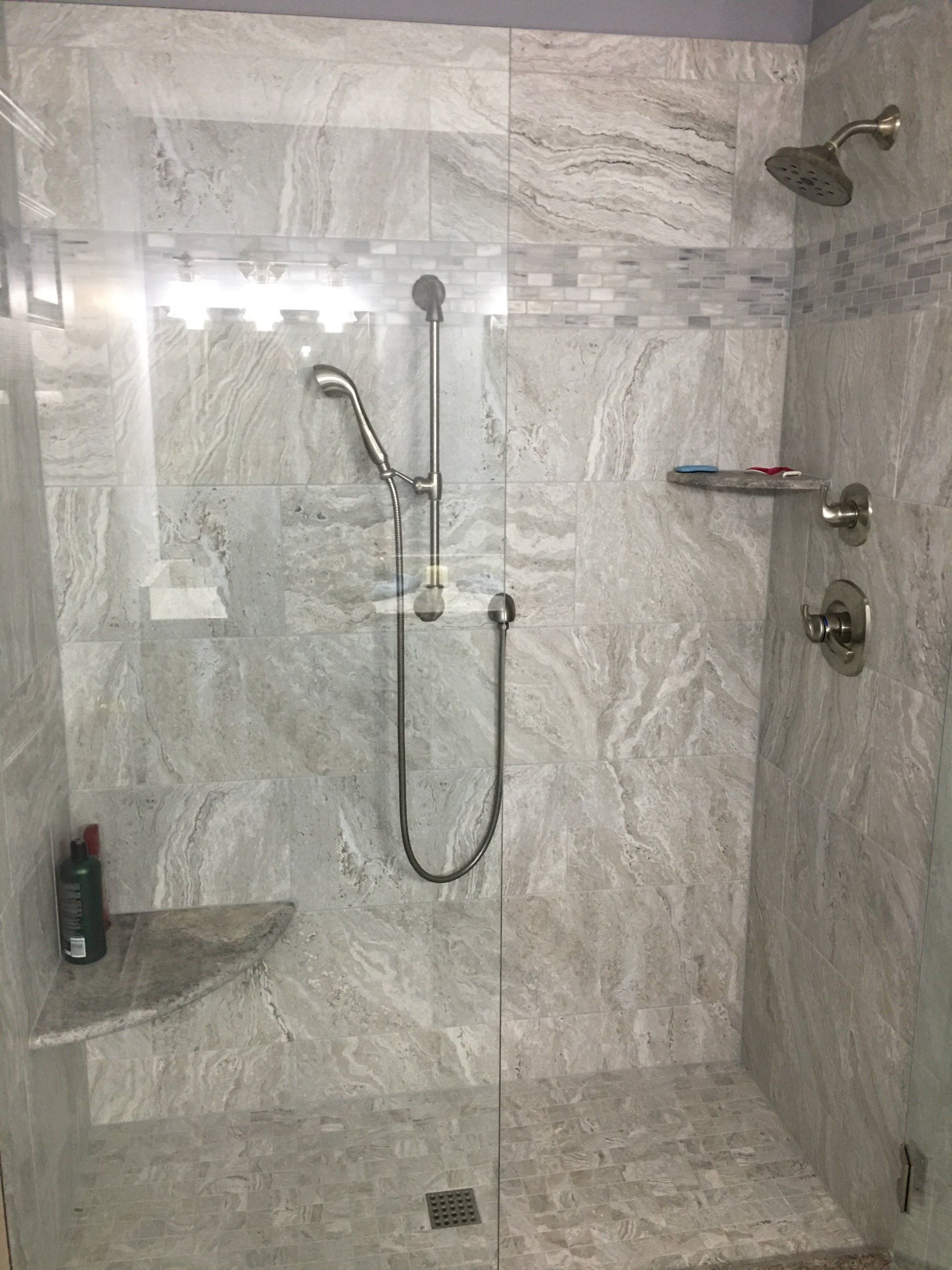 Shower with gray marble-like tile, glass door, handheld and rain shower heads, and a corner shelf.