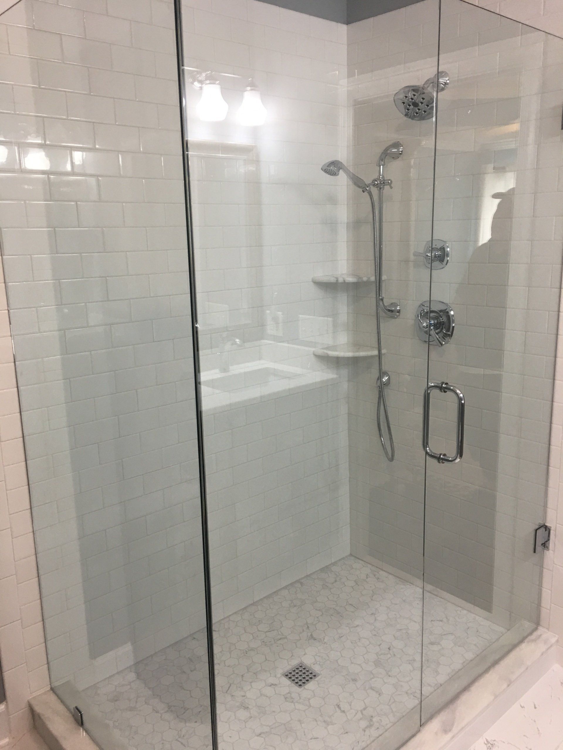 Modern glass shower with white tile walls, stone floor, and chrome fixtures.