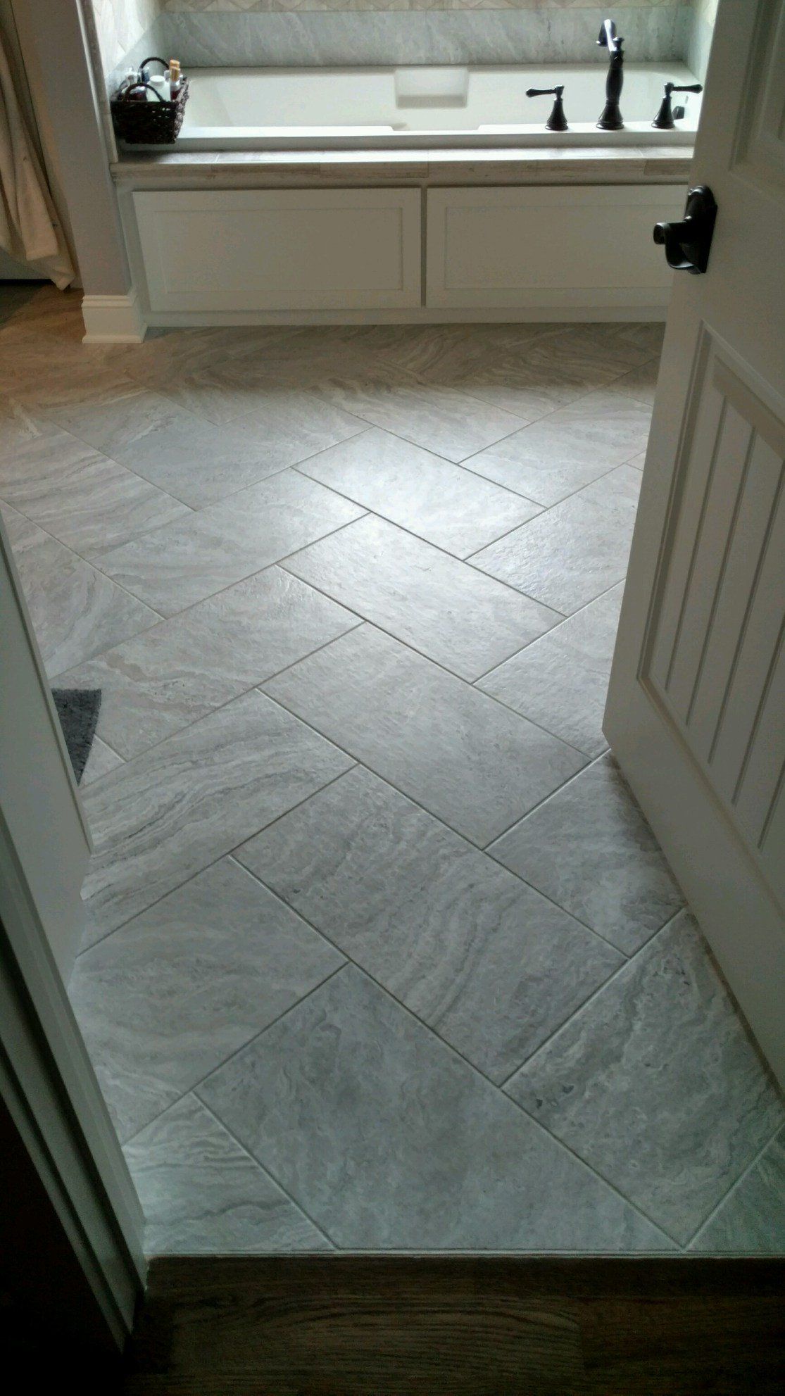 Gray tiled bathroom floor with herringbone pattern, leading to a white tub.
