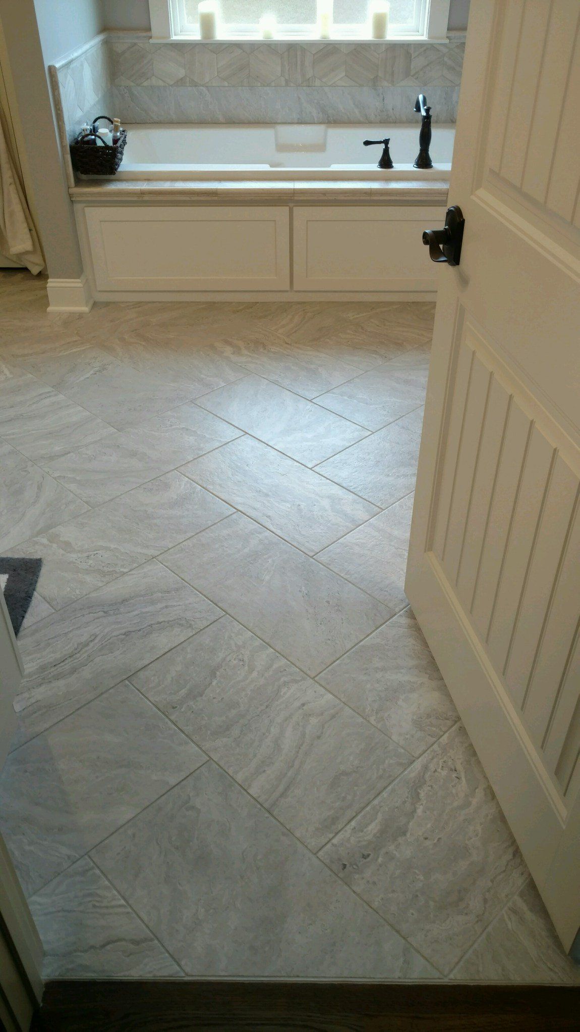 Bathroom with light grey tile flooring, white bathtub, and partially open door.