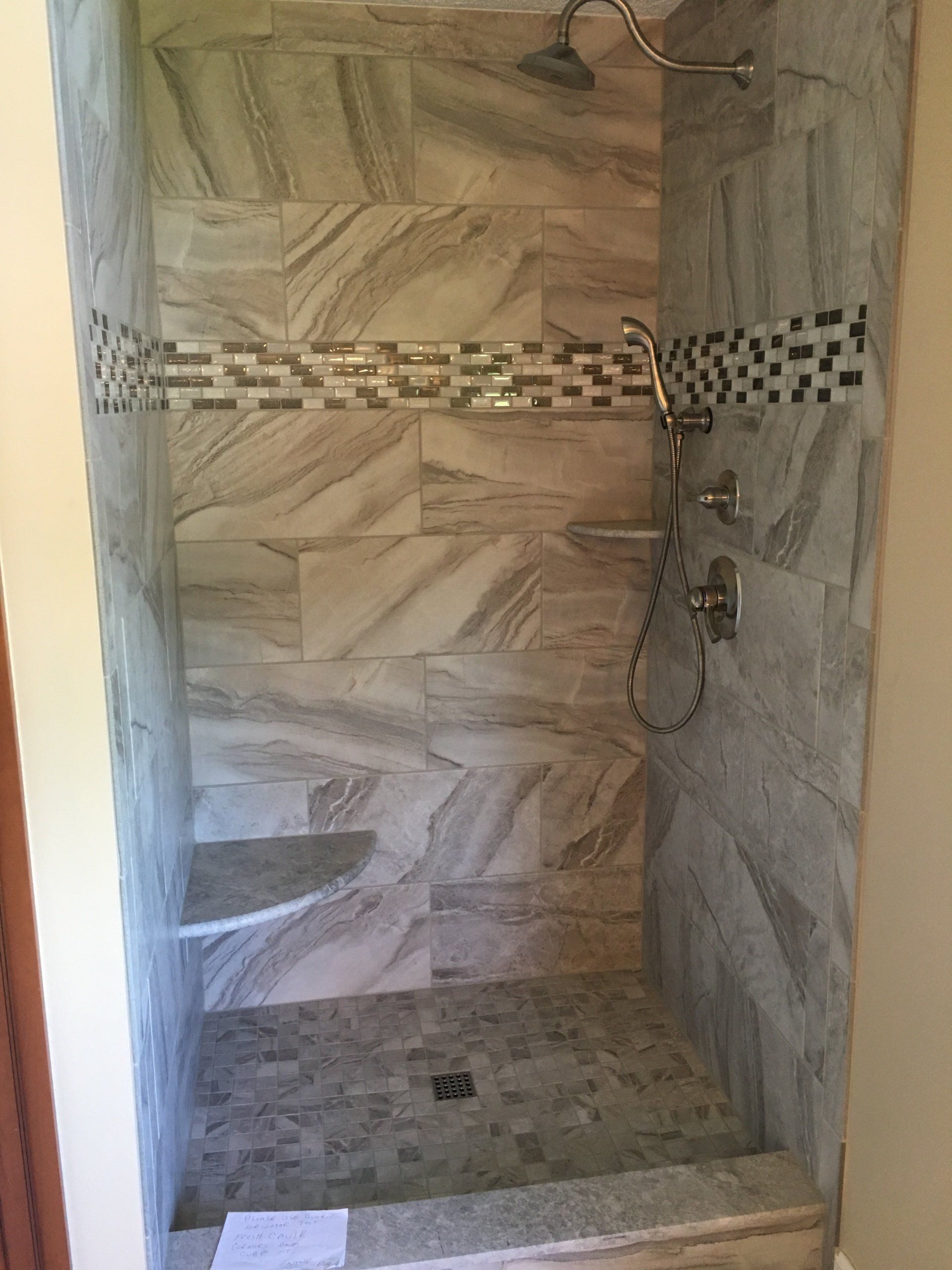 Tiled shower with pebble floor, bench, and decorative horizontal tile strip. Gray and white marble-look tiles.