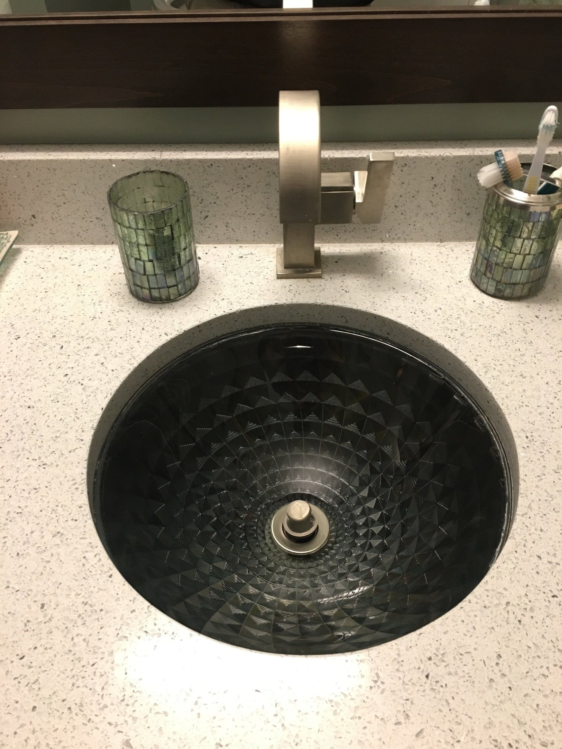 Black textured glass sink on speckled white countertop with brushed nickel faucet.