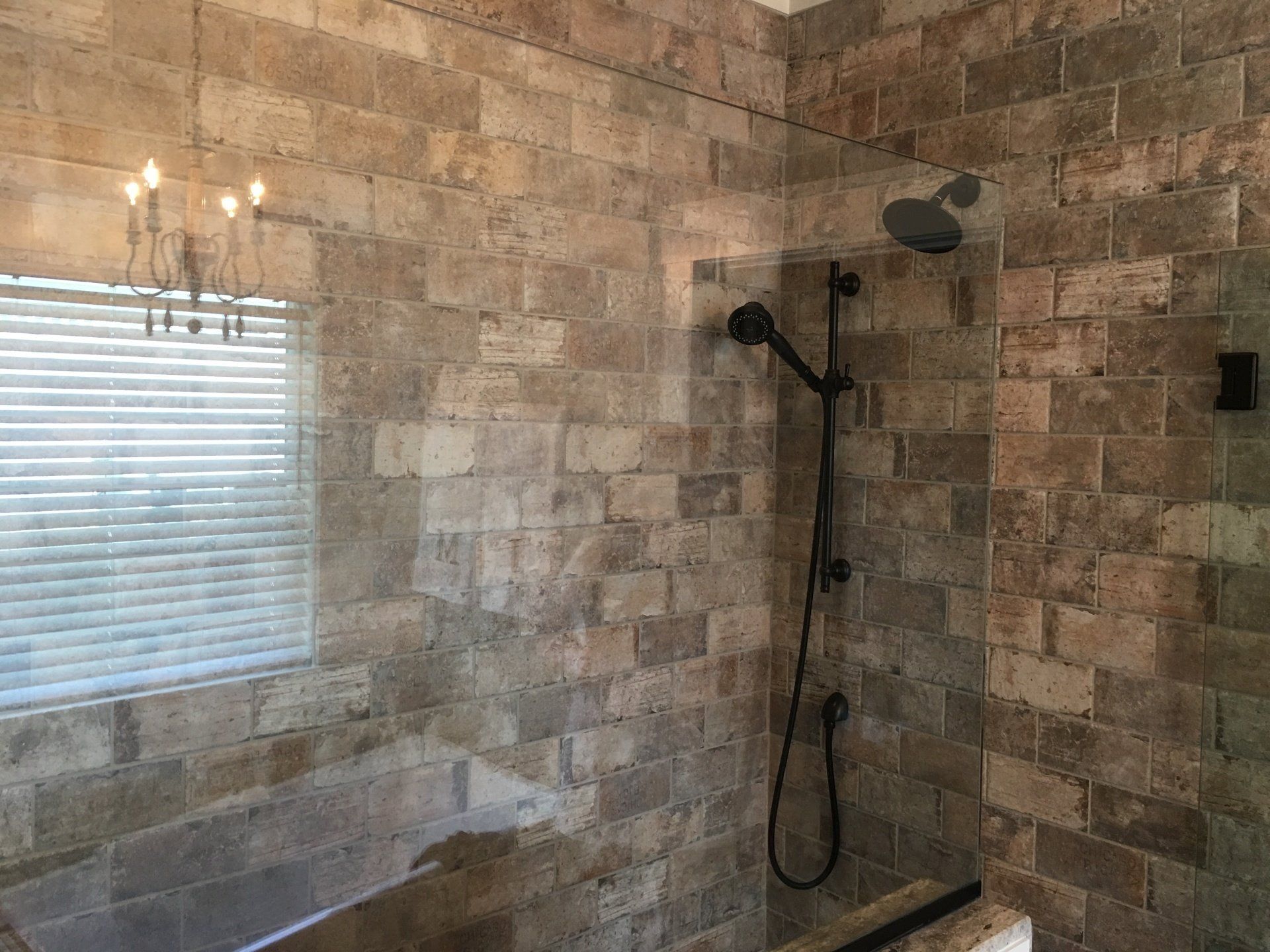 Bathroom with stone tile walls, black shower fixtures, and a window with blinds.