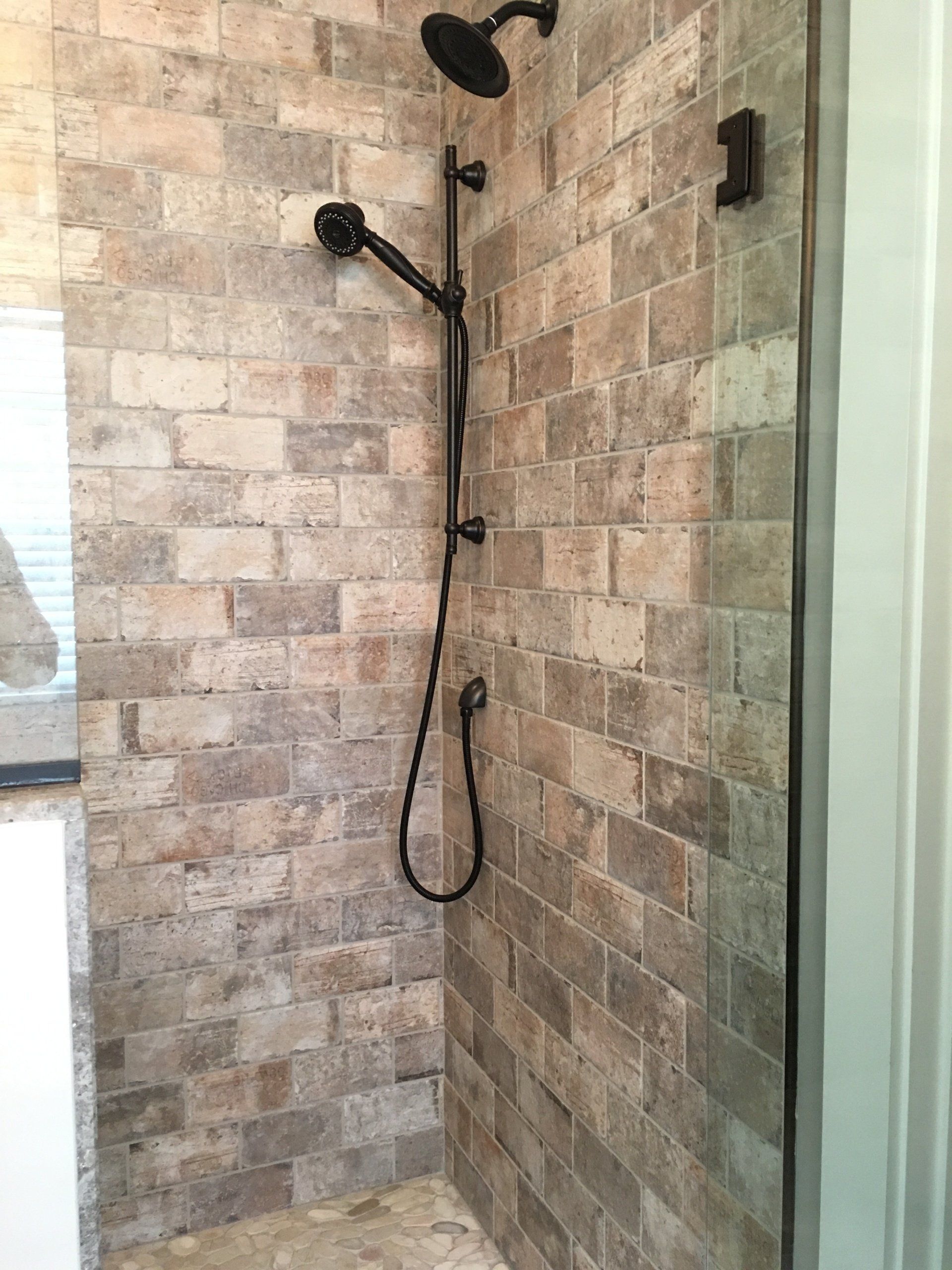 Shower with stone-look tiled walls, black shower fixtures, and a glass door frame.