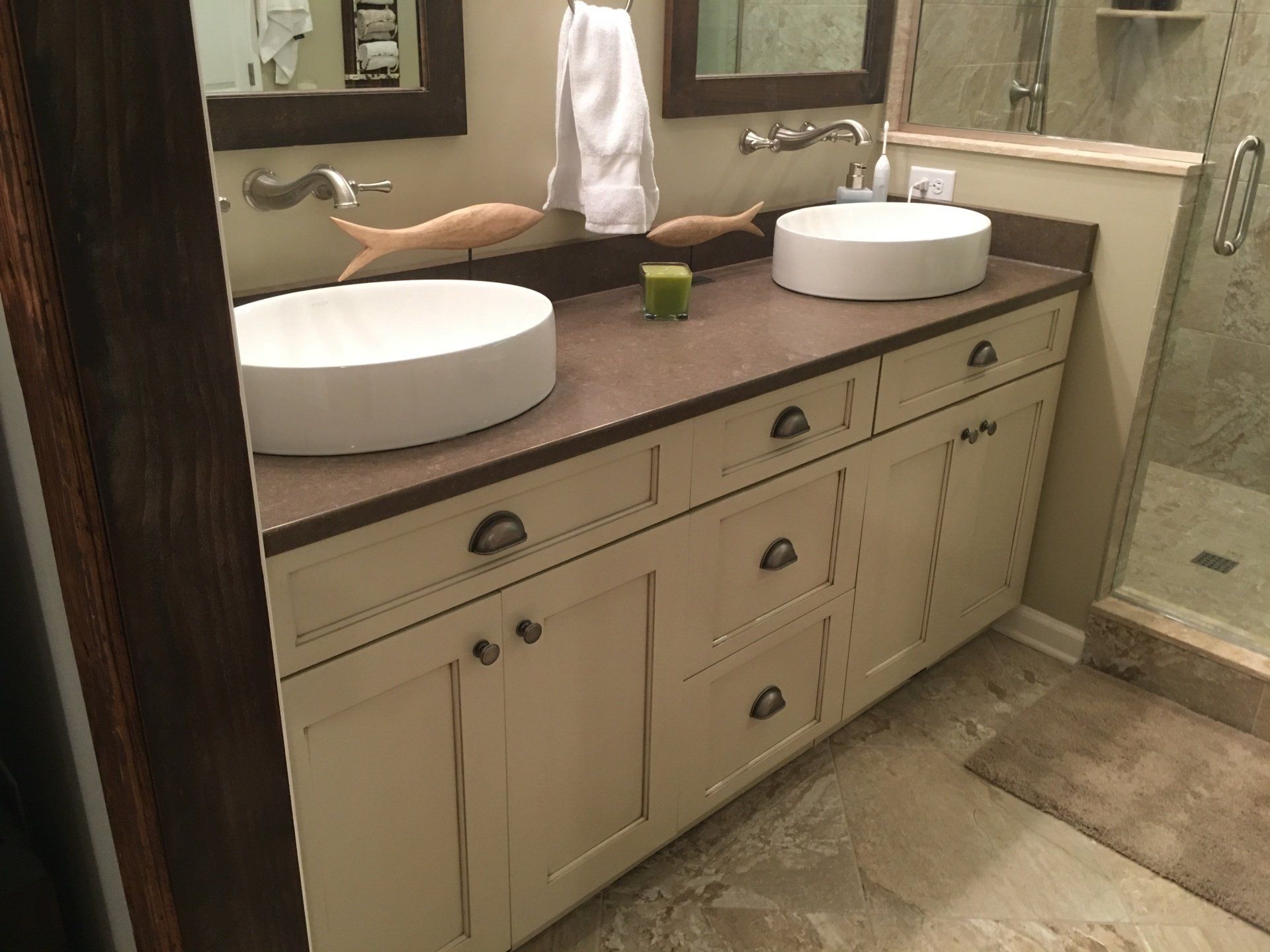 Bathroom with double sinks, cream cabinets, brown countertop, and a shower.