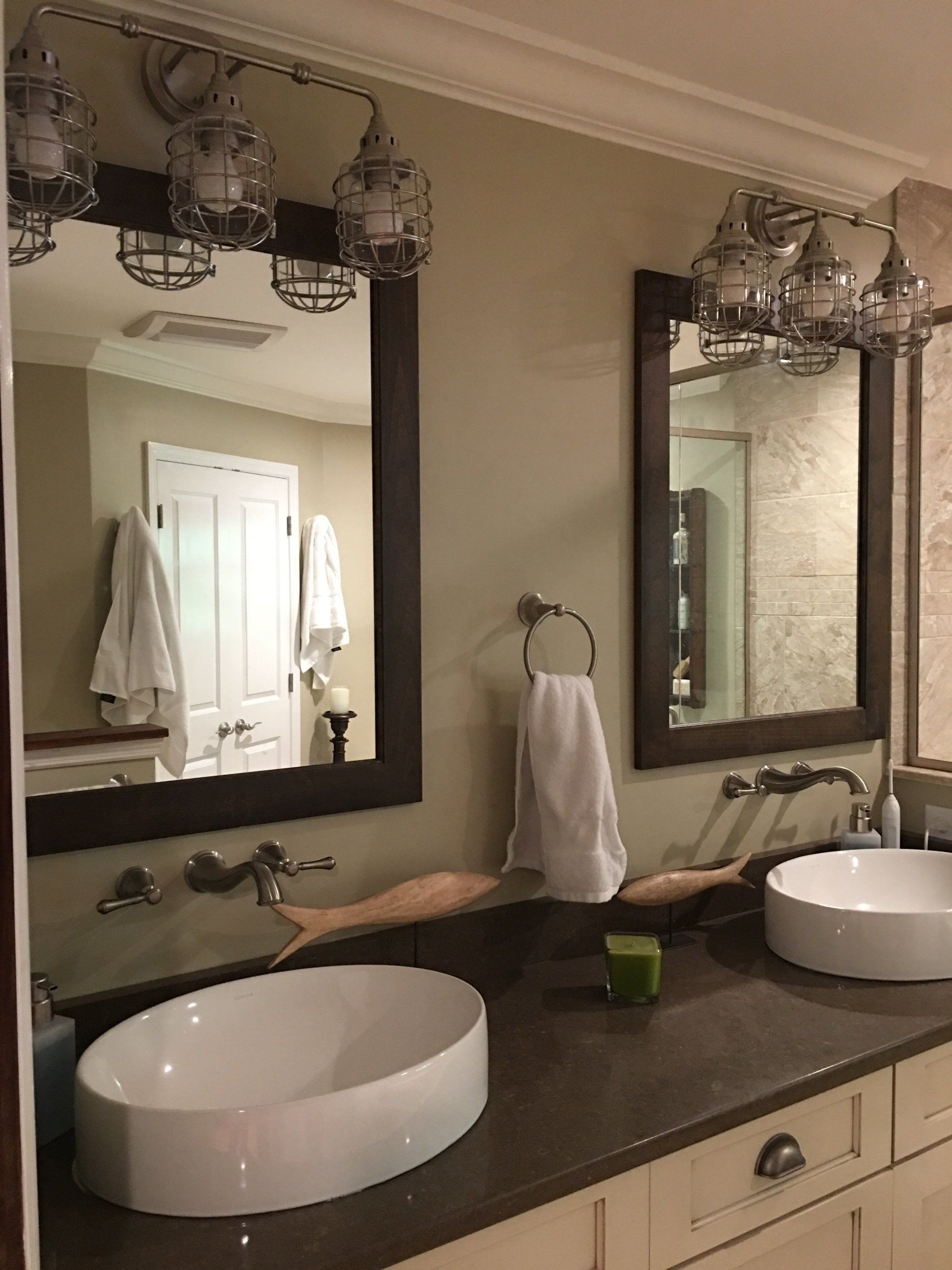Bathroom with two mirrors, vessel sinks, and industrial-style lighting fixtures. Light green walls and white cabinetry.