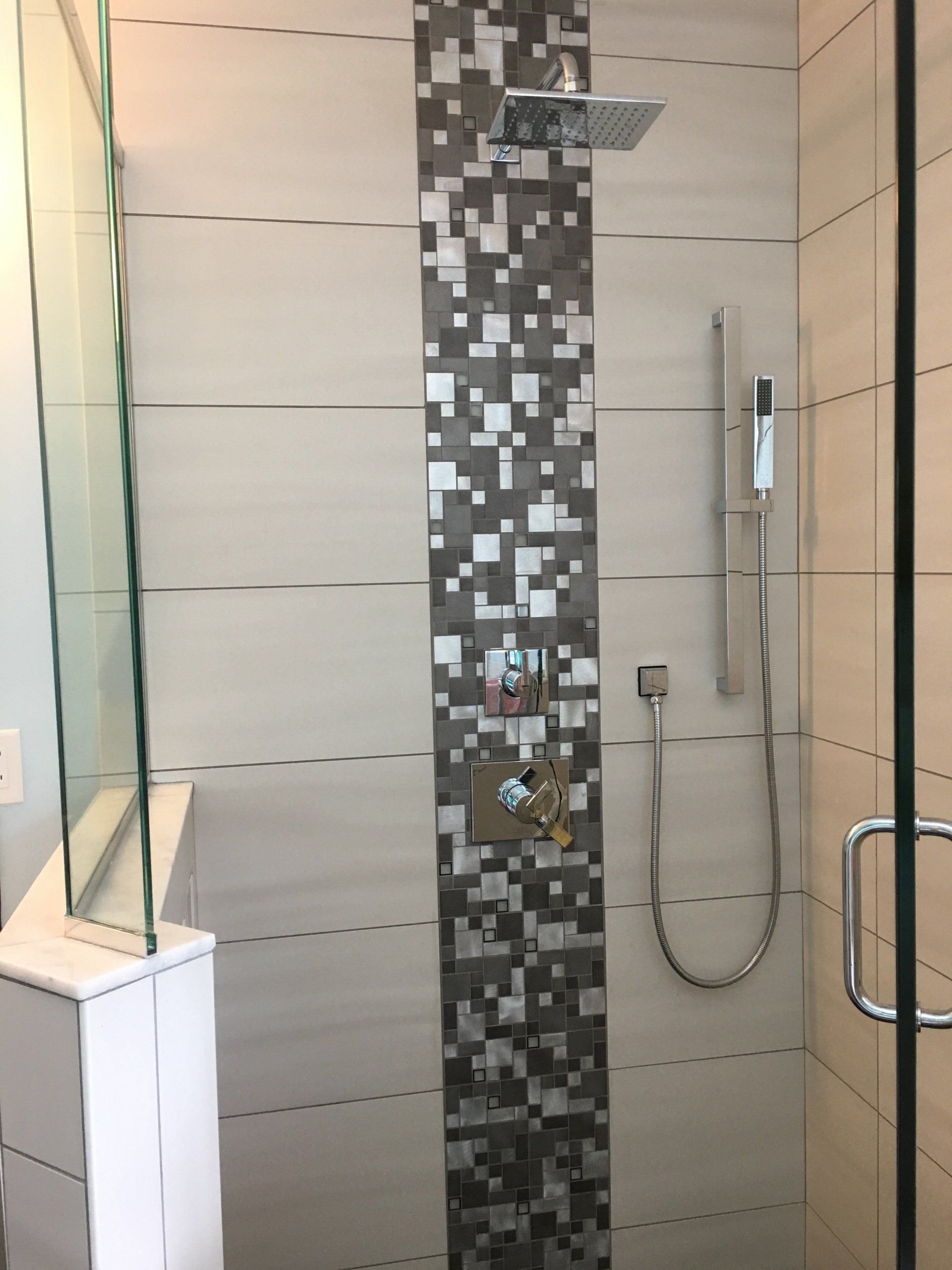 Shower with gray, silver, and white tile and glass door.
