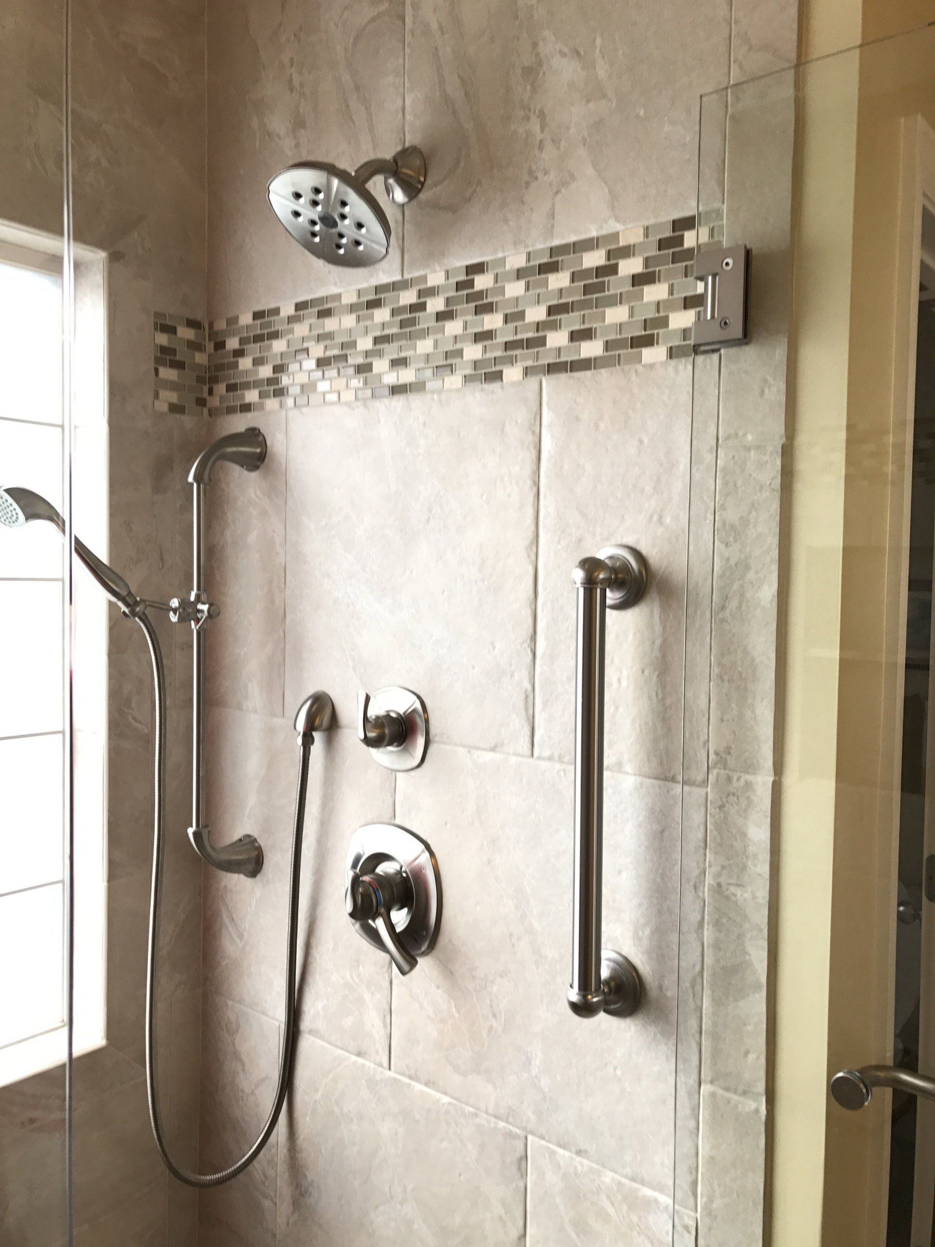 Shower with tile surround, mosaic accent, grab bar, and two showerheads.