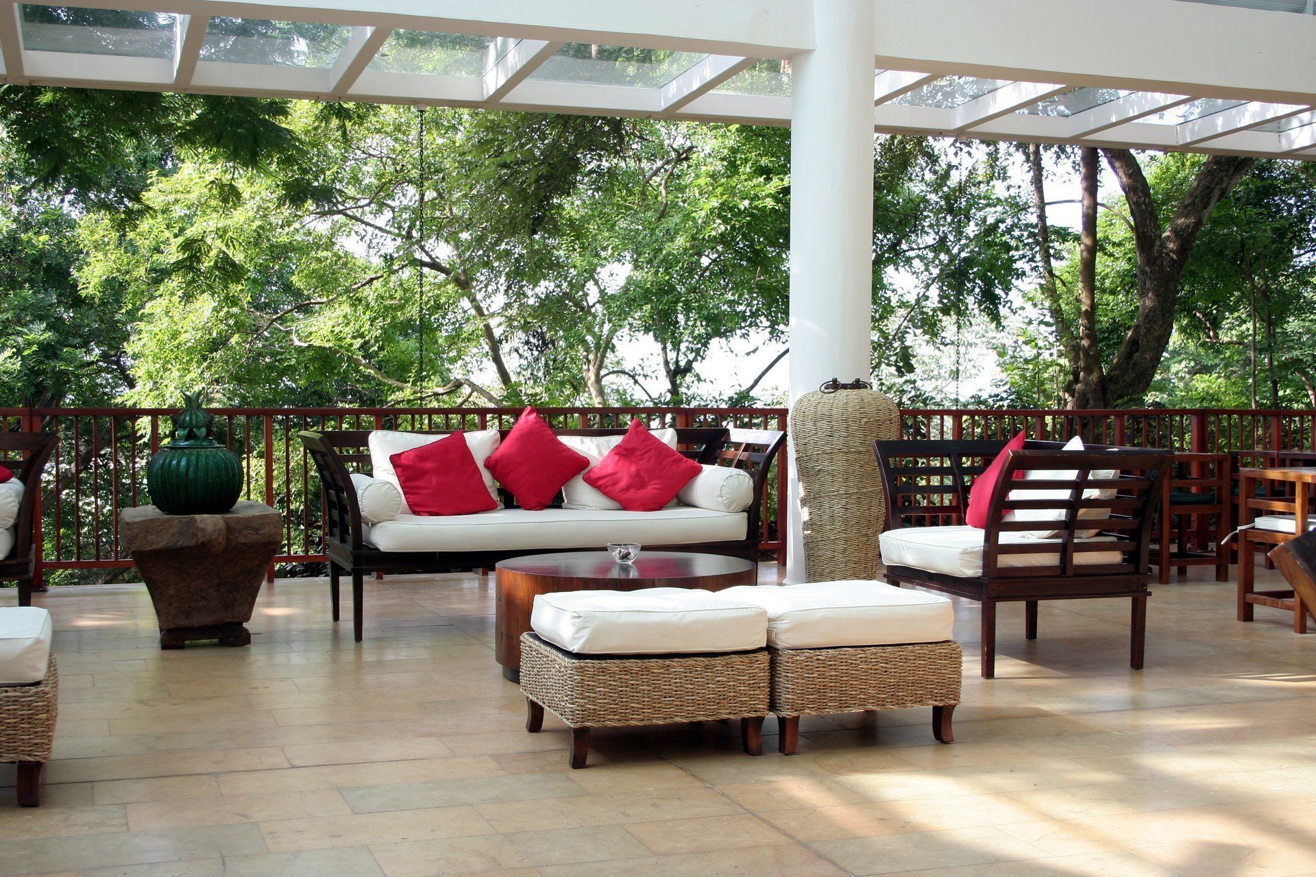 Outdoor lounge area with white and red cushions, wood furniture, and a view of trees.