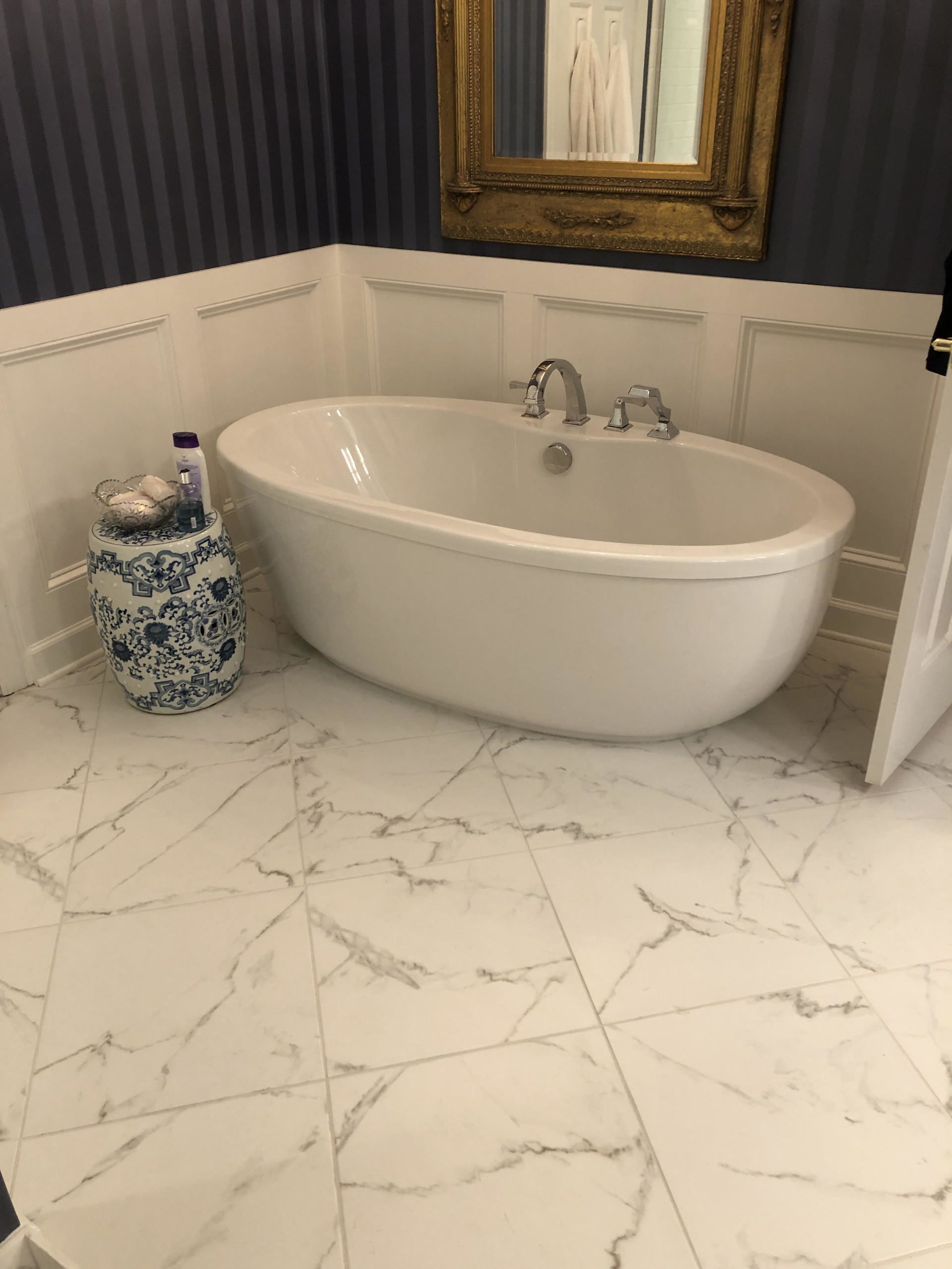 Oval bathtub in a white and marble-tiled bathroom with blue and white decor.
