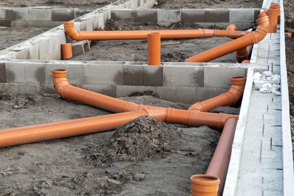 A bunch of orange pipes are laying in the dirt